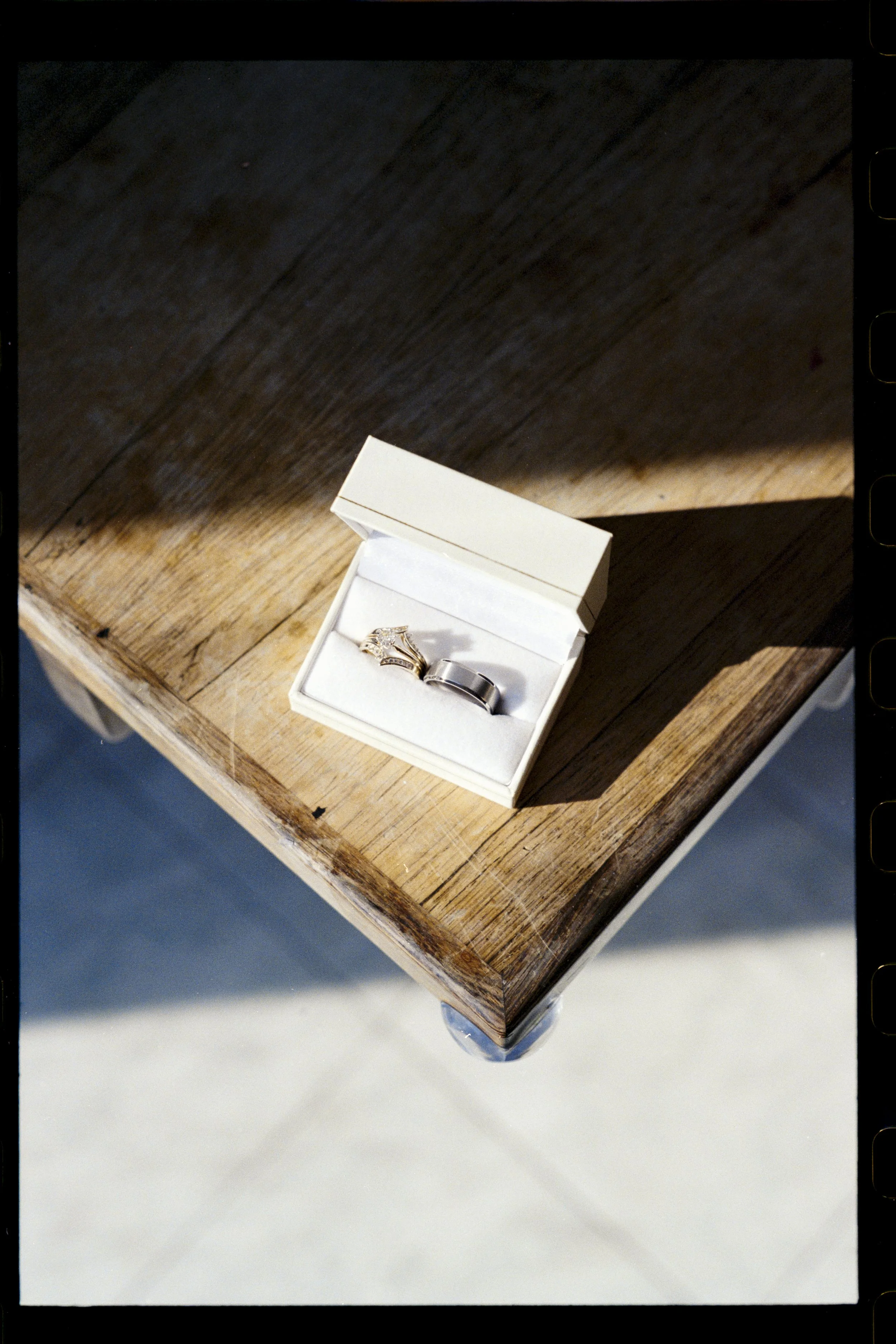 A jewelry box with two rings on a wooden table.