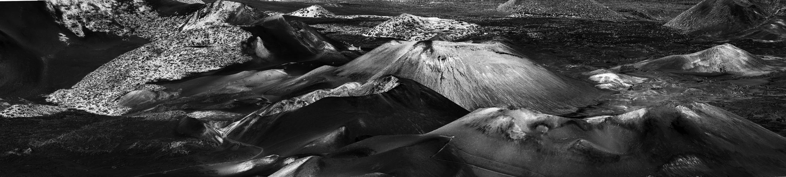 Black and white aerial photograph of volcanic mountains with multiple craters and volcanic surface textures.