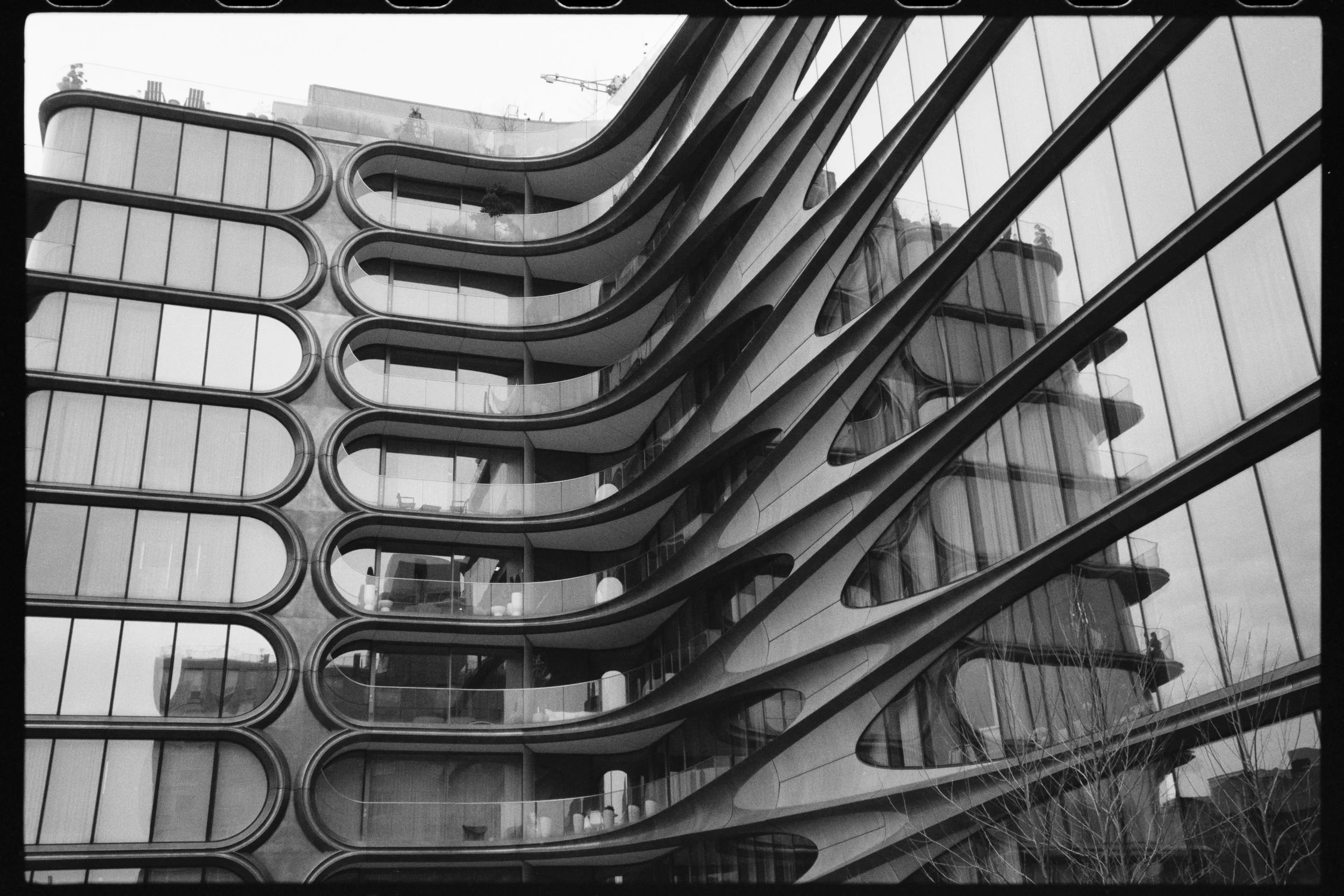A modern architectural building with multiple rounded balconies and glass windows, reflecting neighboring structures.