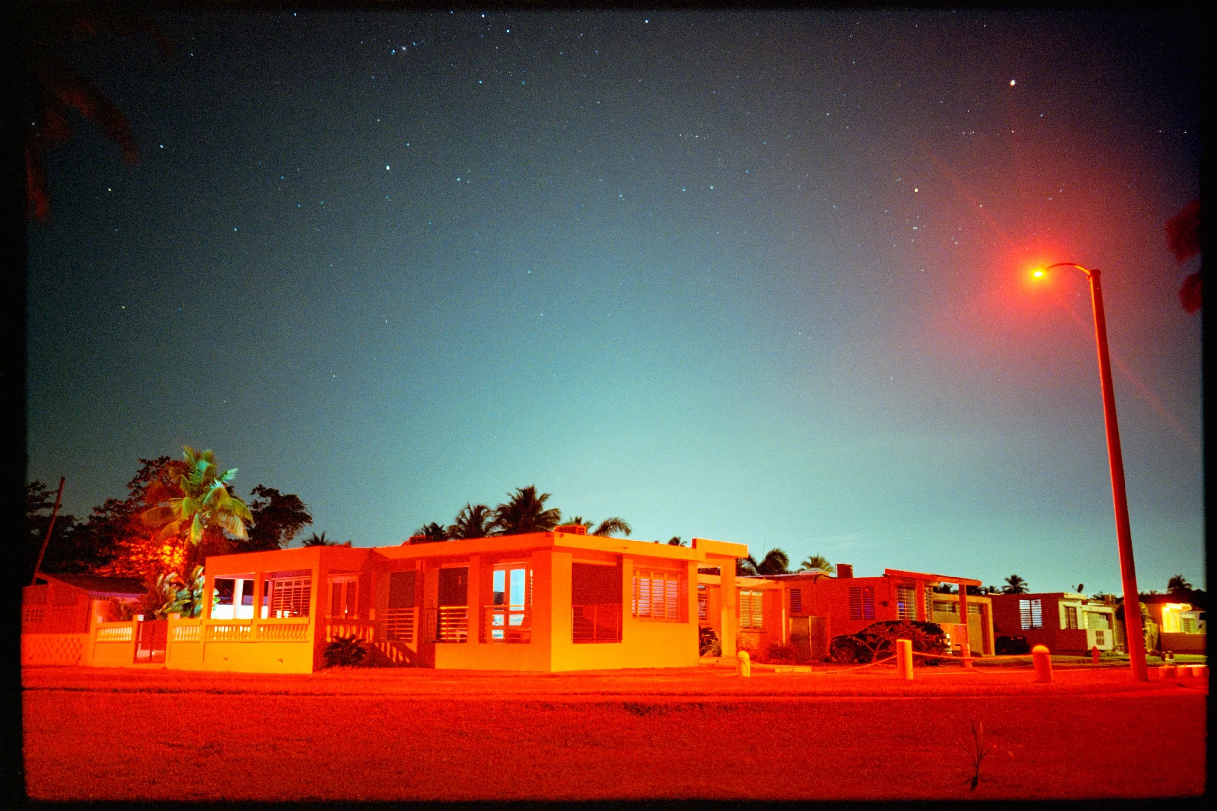 Night scene of modern tropical buildings under a starry sky, illuminated by streetlights.