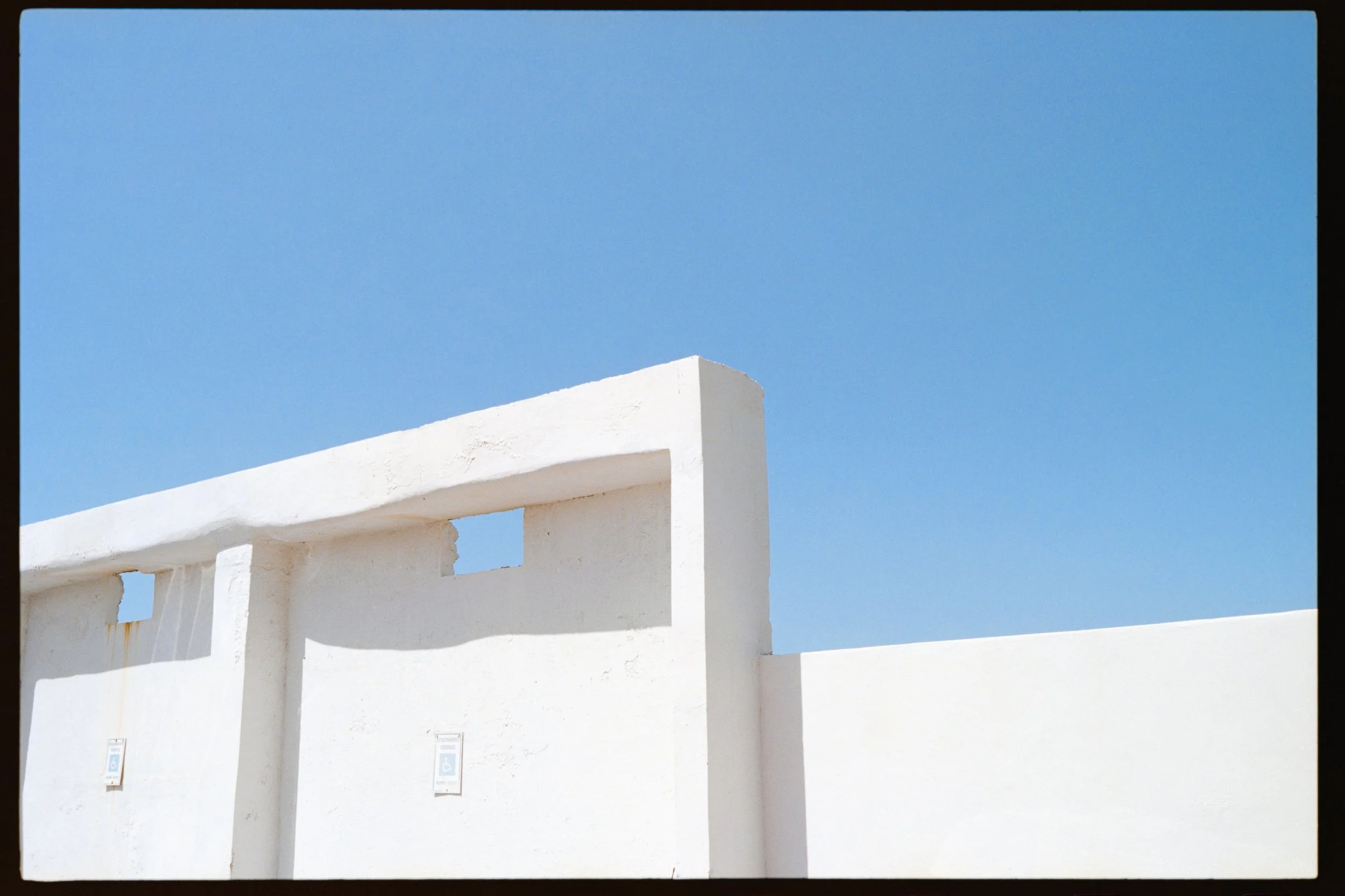 White building with arches and blue sky in the background, two accessible parking signs at the bottom.