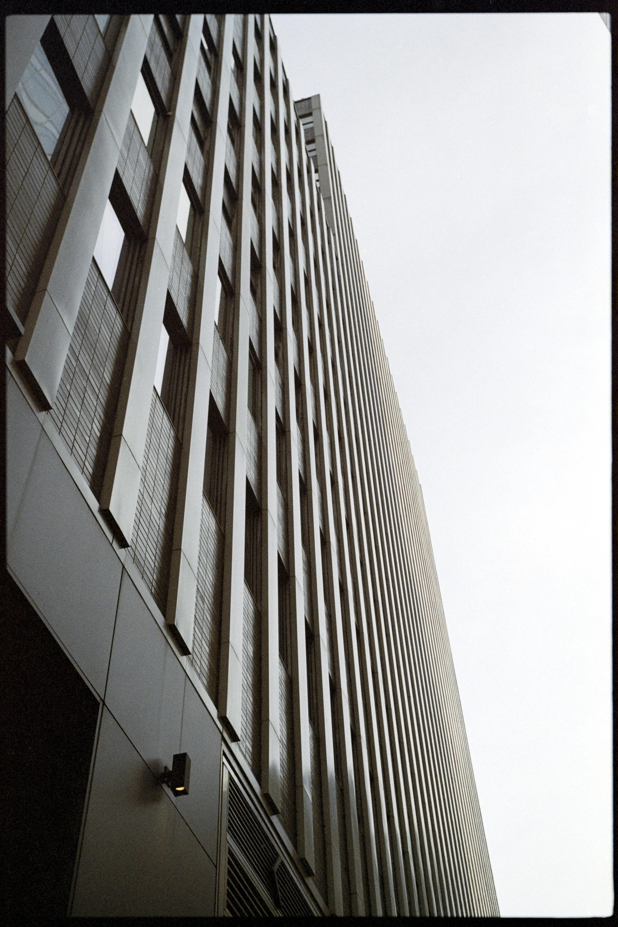 Close-up view of a modern high-rise building with vertical metal slats and glass windows, taken from below against a cloudy sky.