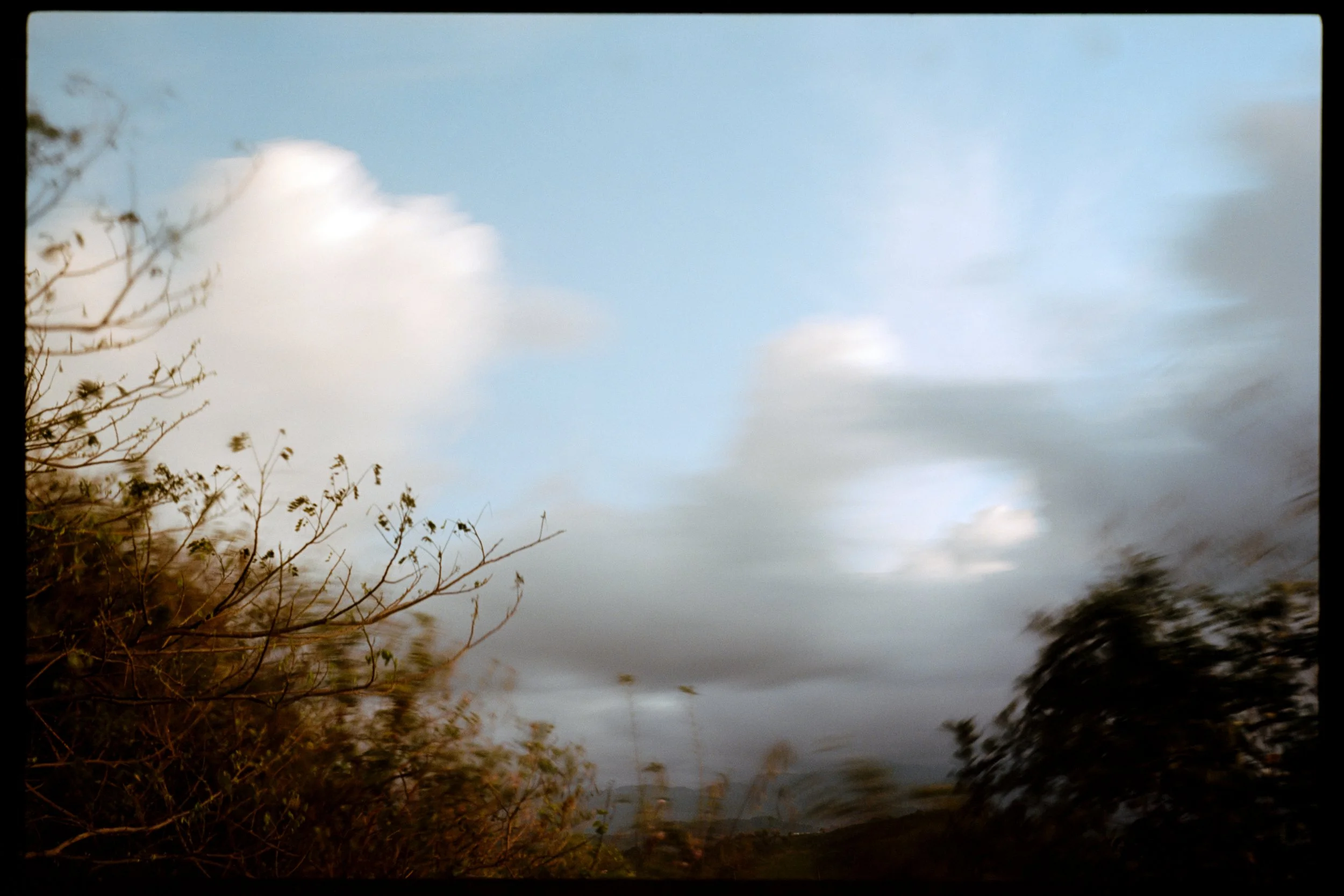 Overcast sky with a few clouds, view of leafless tree branches in the foreground.