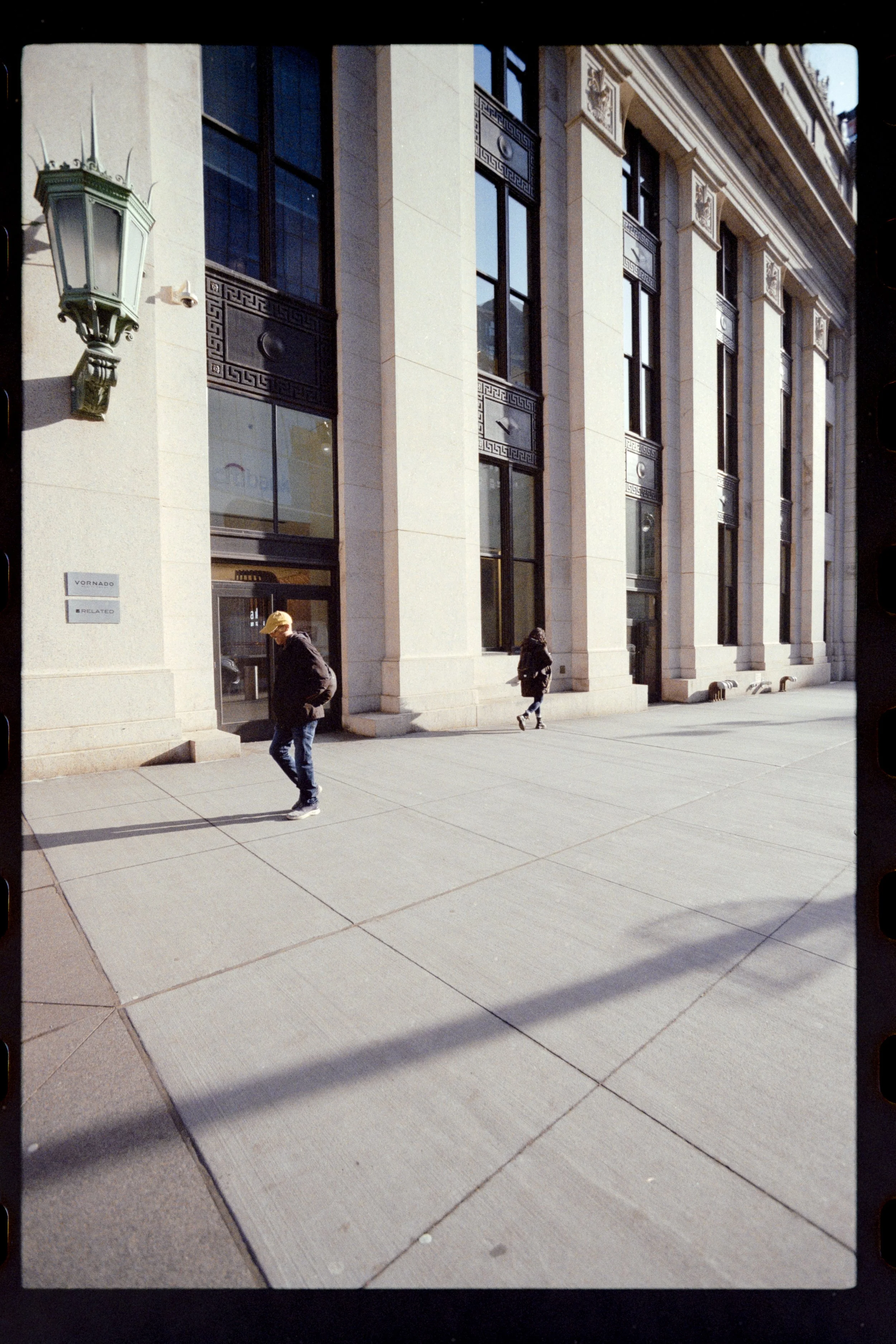 Street view with people walking in front of a large, ornate building with tall windows and decorative columns