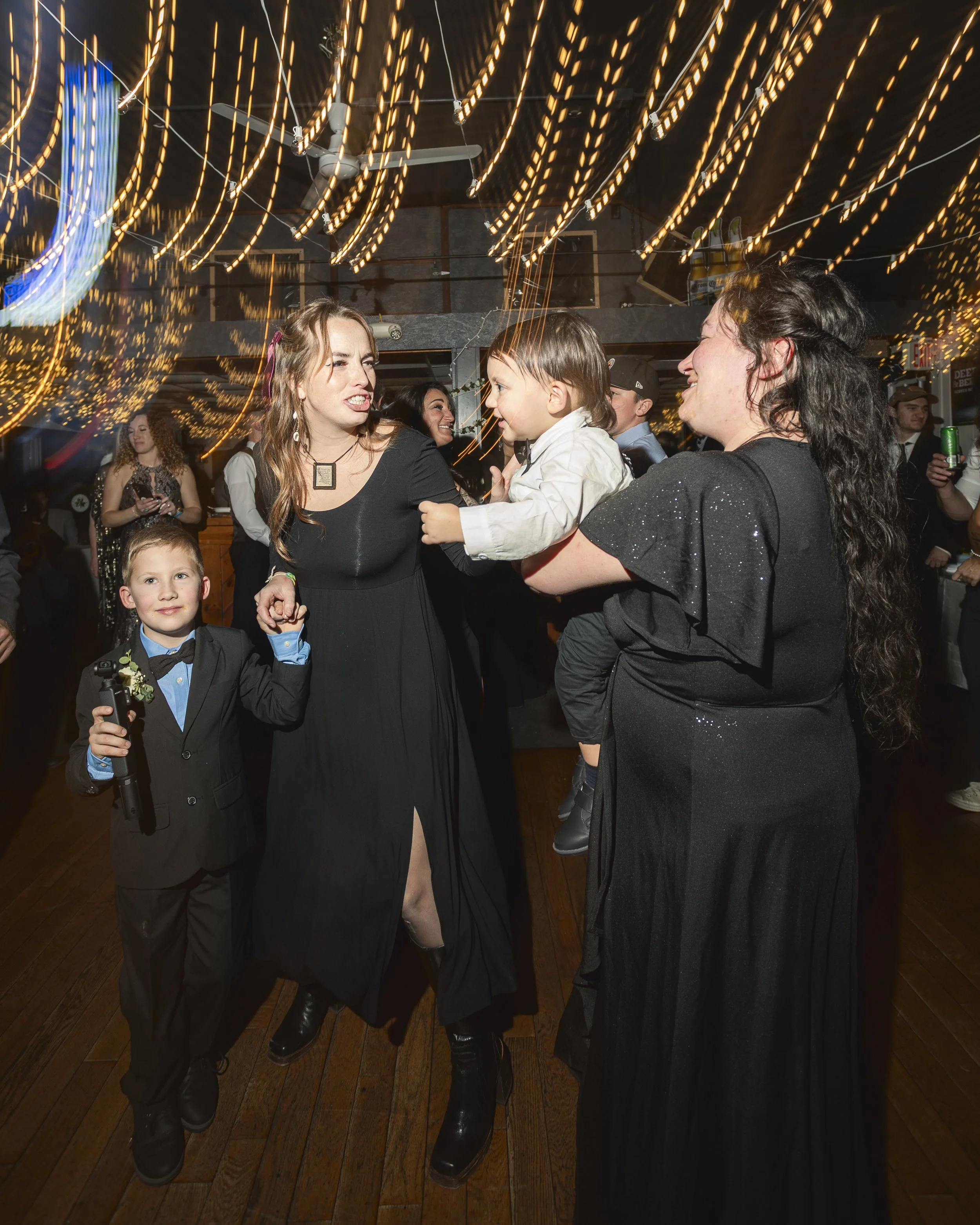 People dancing and celebrating at a party with string lights and a wooden floor.