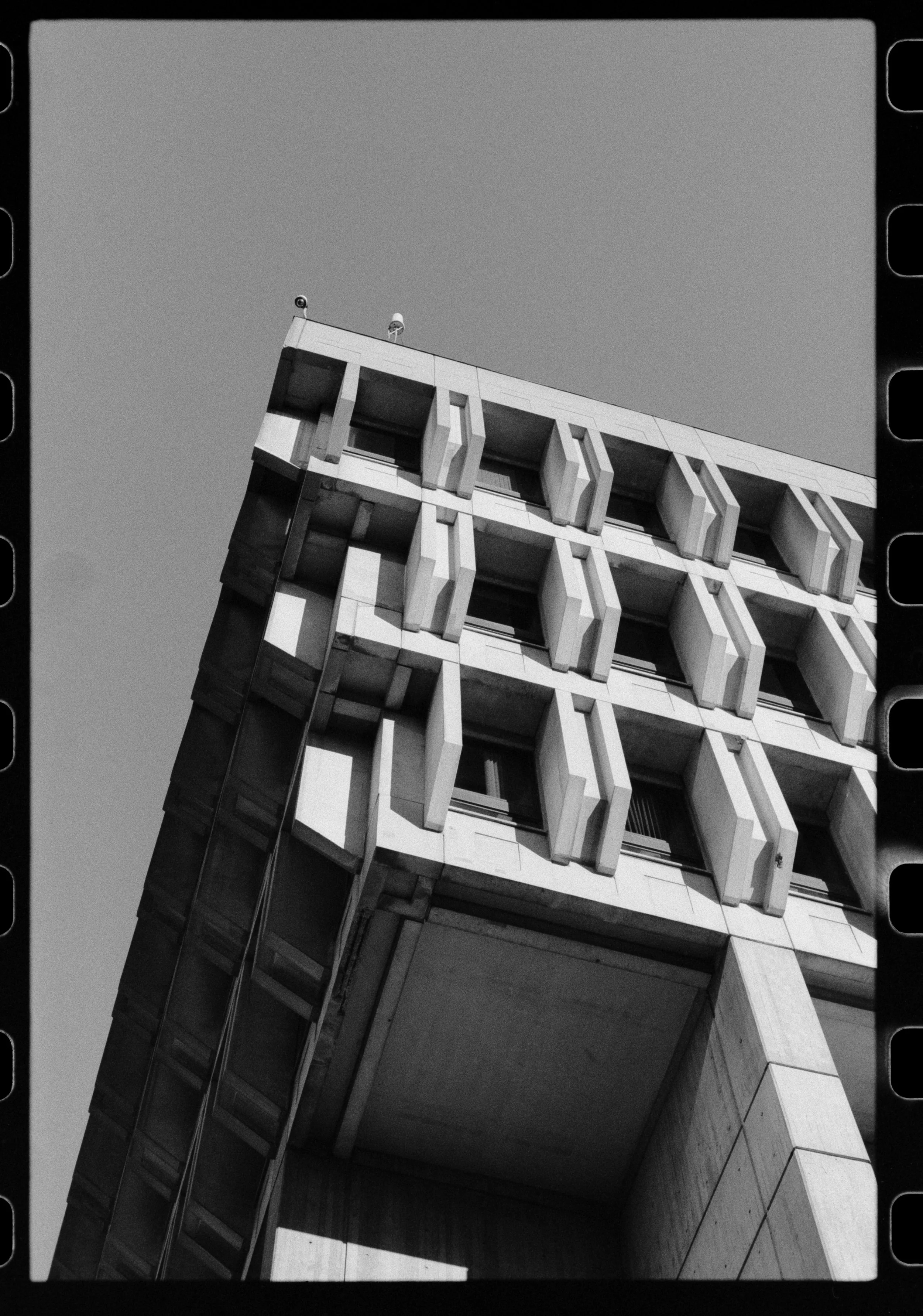 Black and white photo of a modern apartment building with balconies and windows, taken from a low angle.
