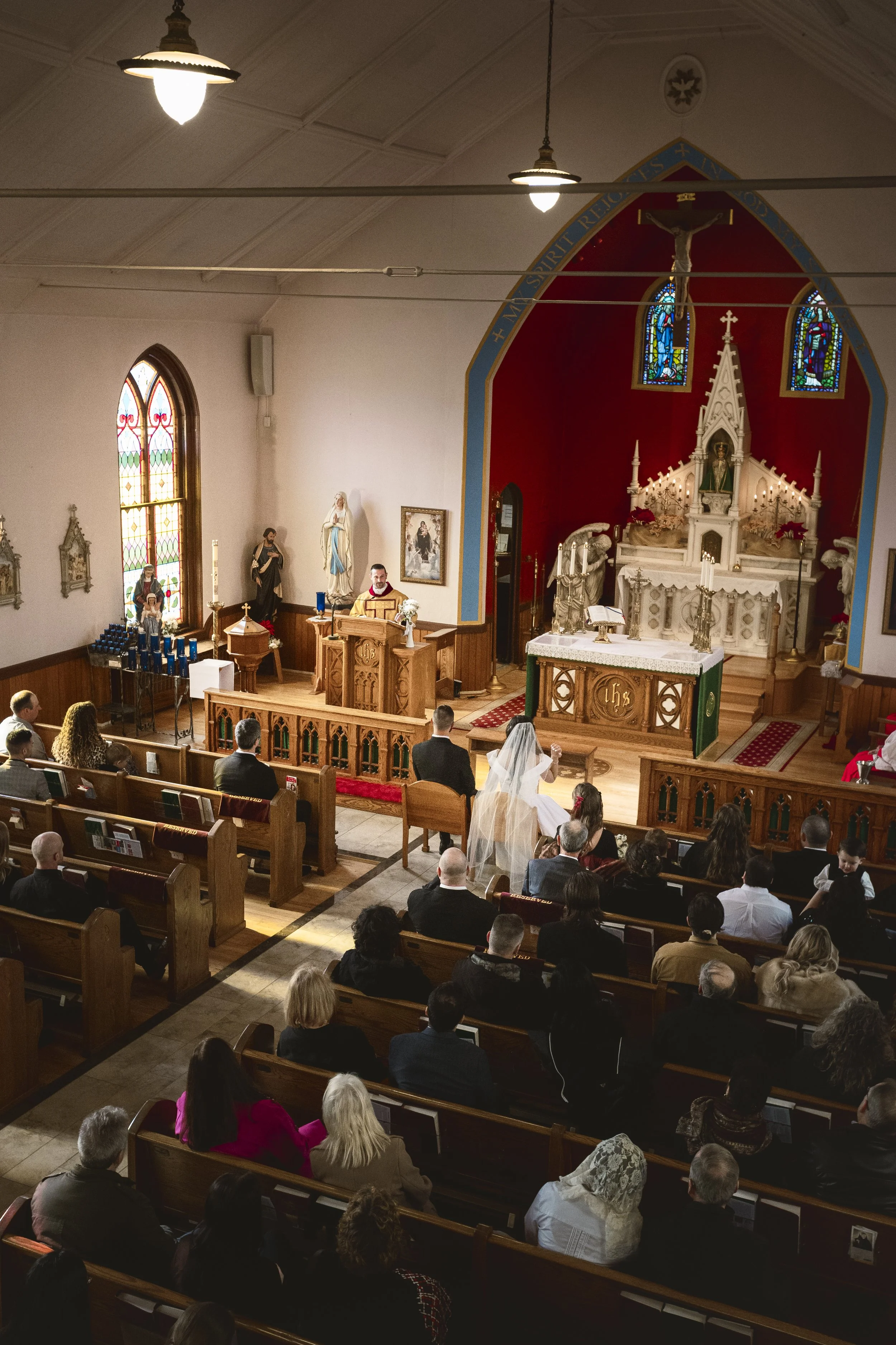 A wedding ceremony inside a church with a bride and groom kneeling at the altar, surrounded by guests seated in pews.