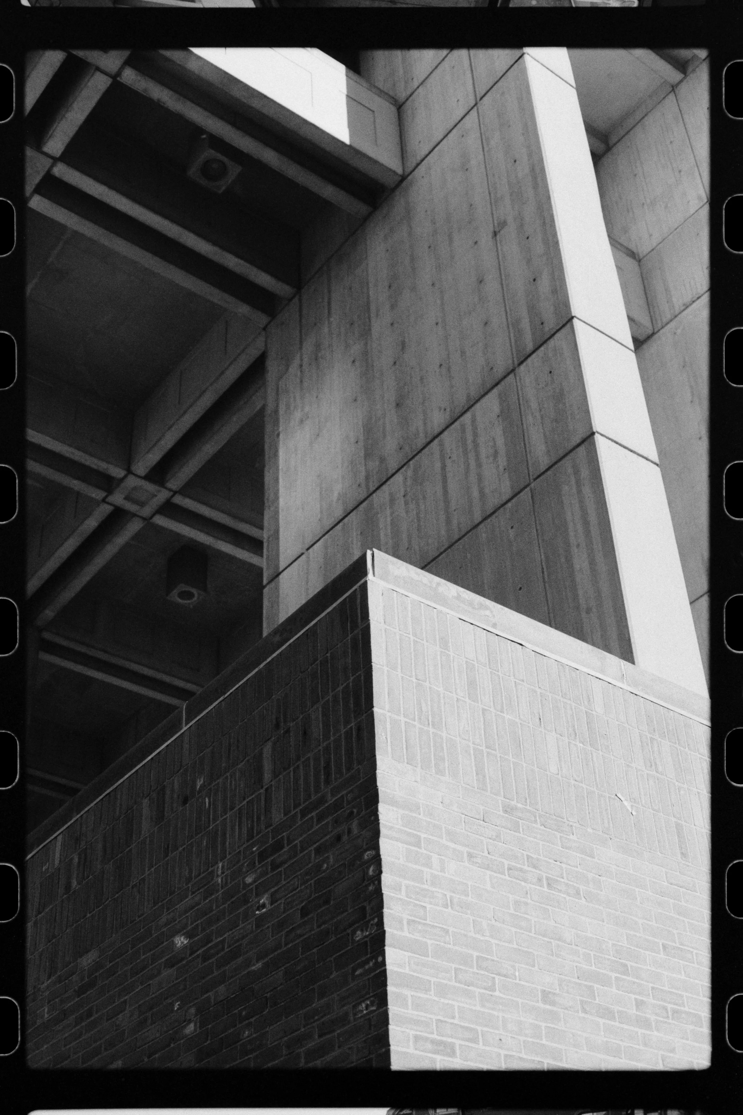 Black and white photo of intersecting modern building walls with different textures, including brick, concrete, and tiled surfaces.