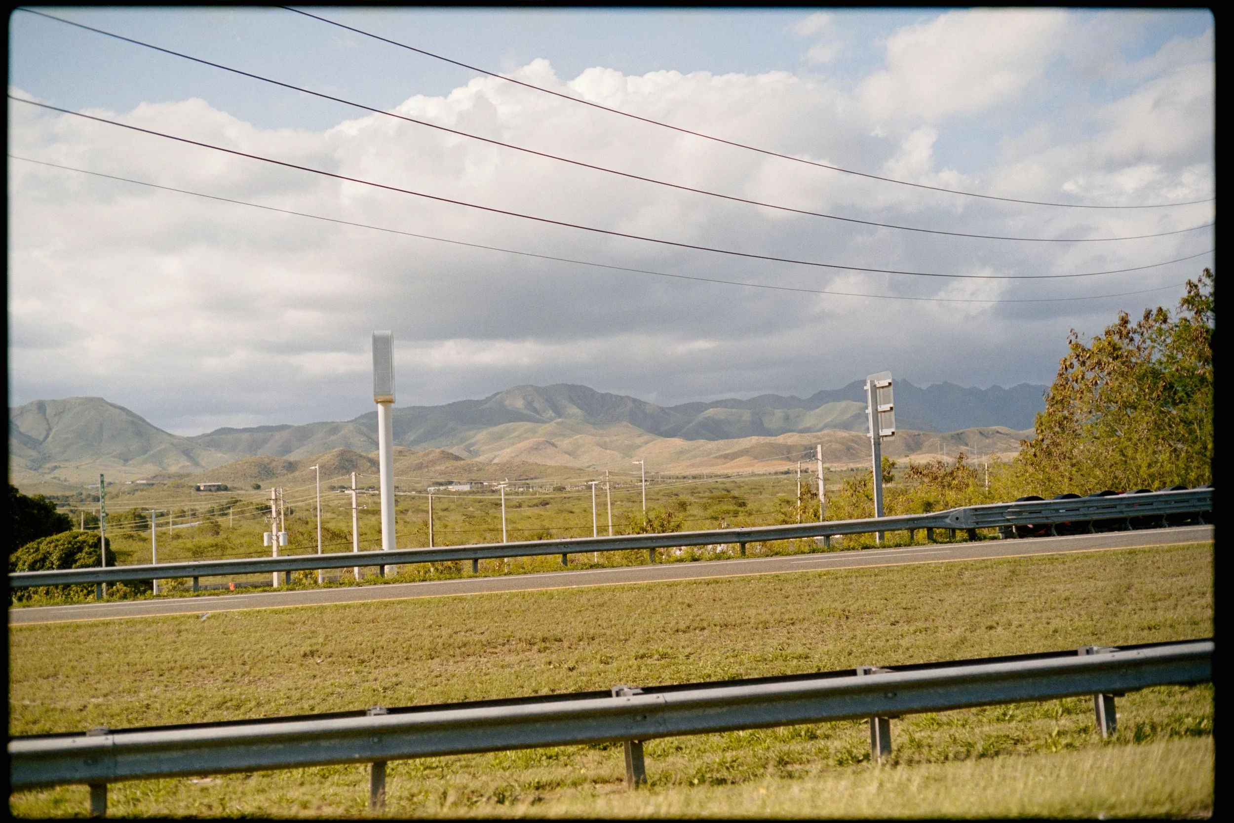 A scenic view of mountains under partly cloudy sky, with power lines and utility poles along the roadside.