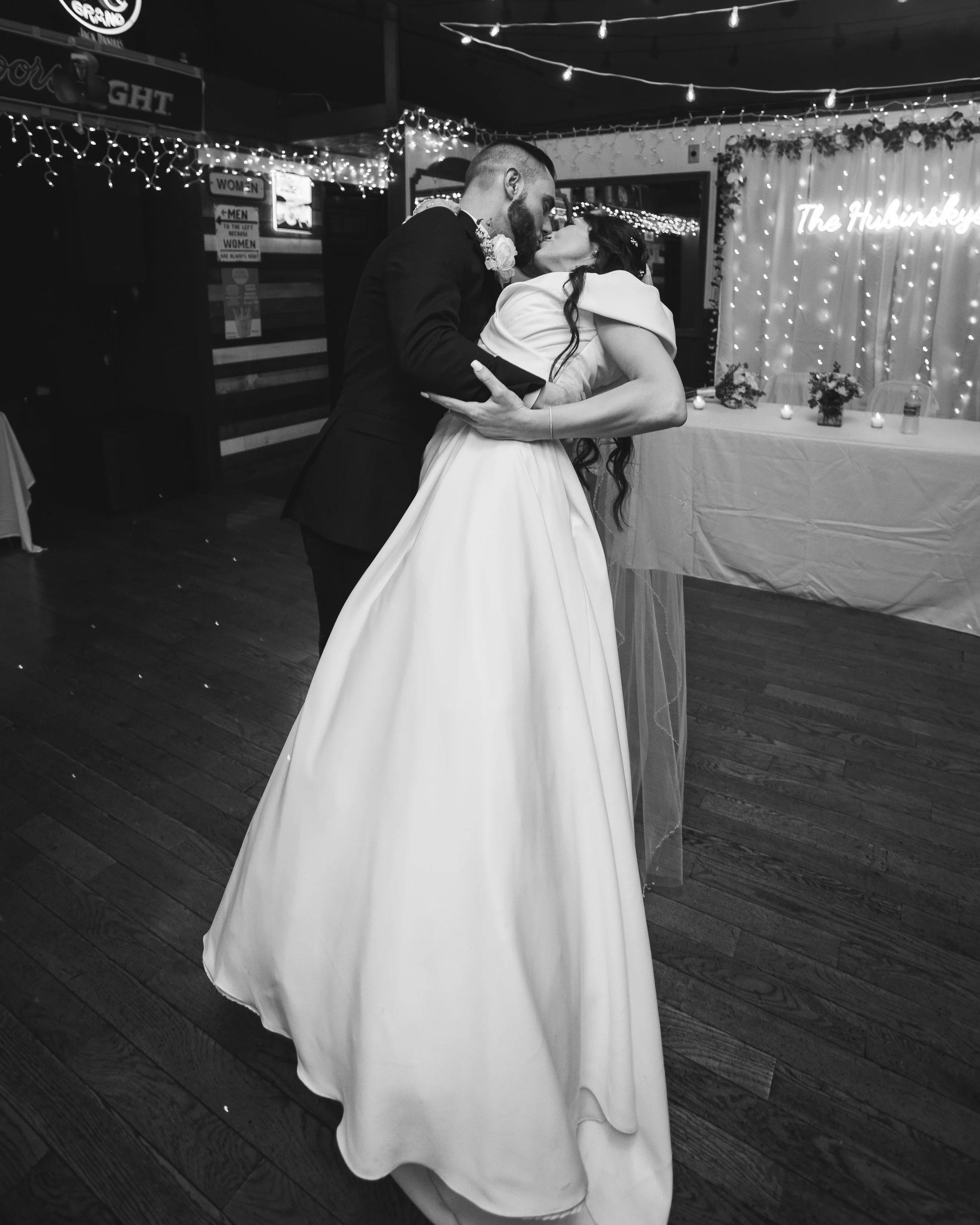 A bride and groom share a dance at their wedding reception, with wedding decorations and string lights in the background.