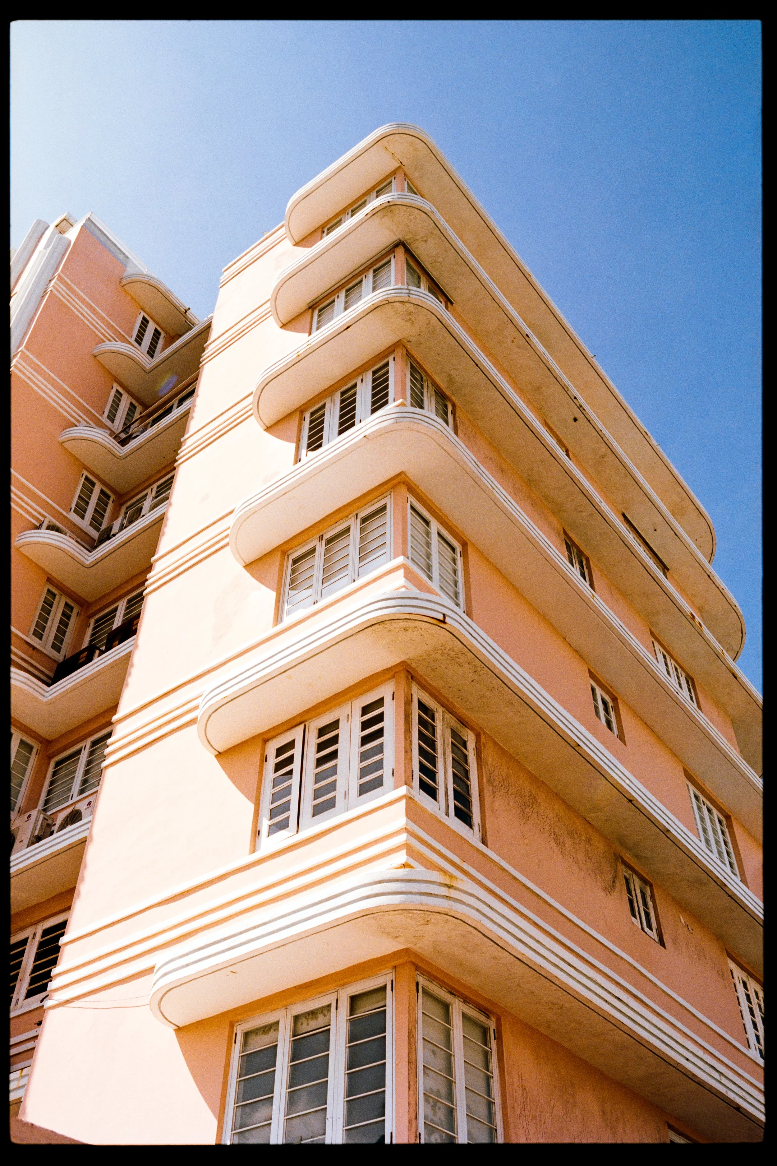 A tall peach-colored apartment building with multiple rounded balconies and white trim, set against a clear blue sky.