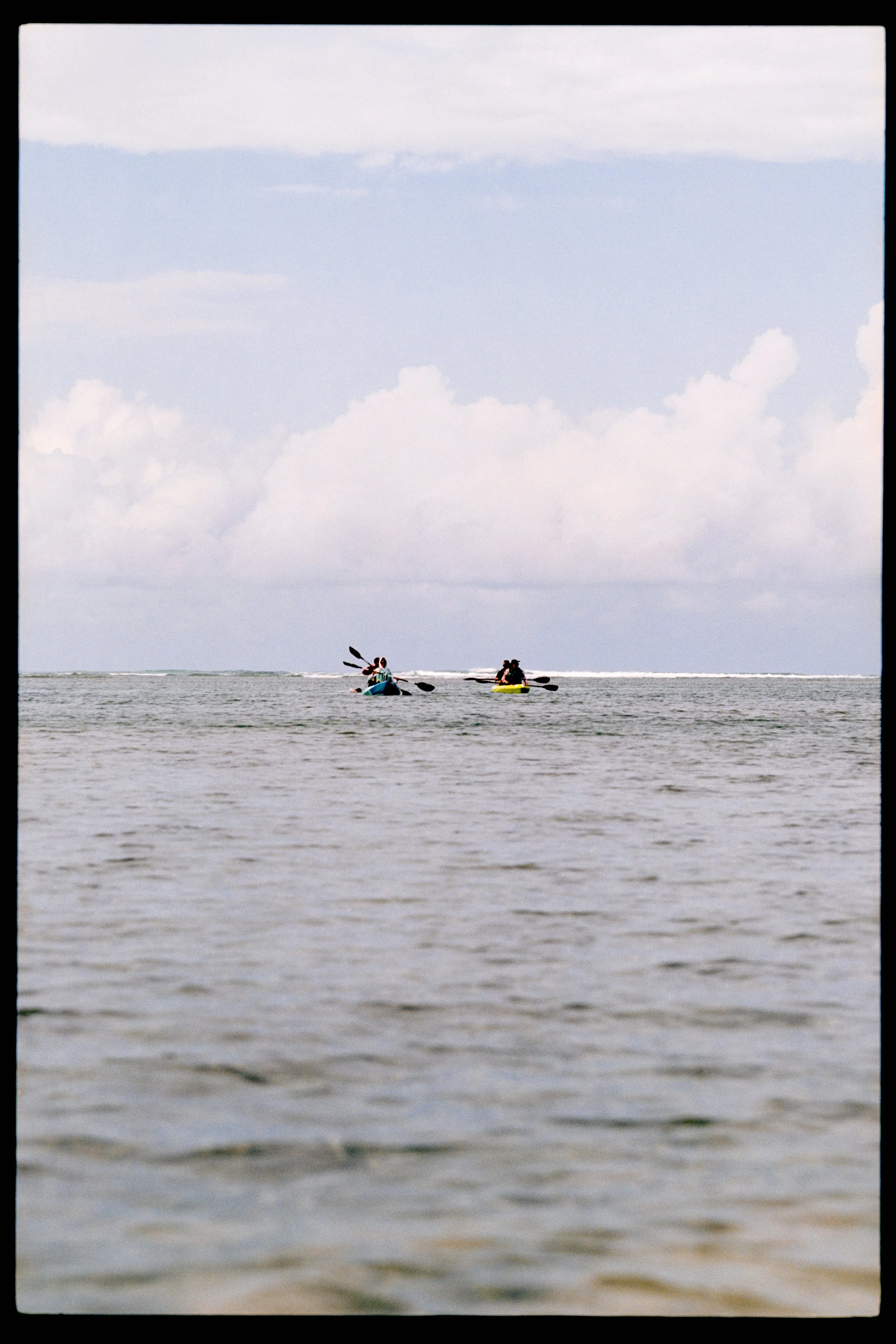 Two people kayaking on a body of water under a partly cloudy sky.