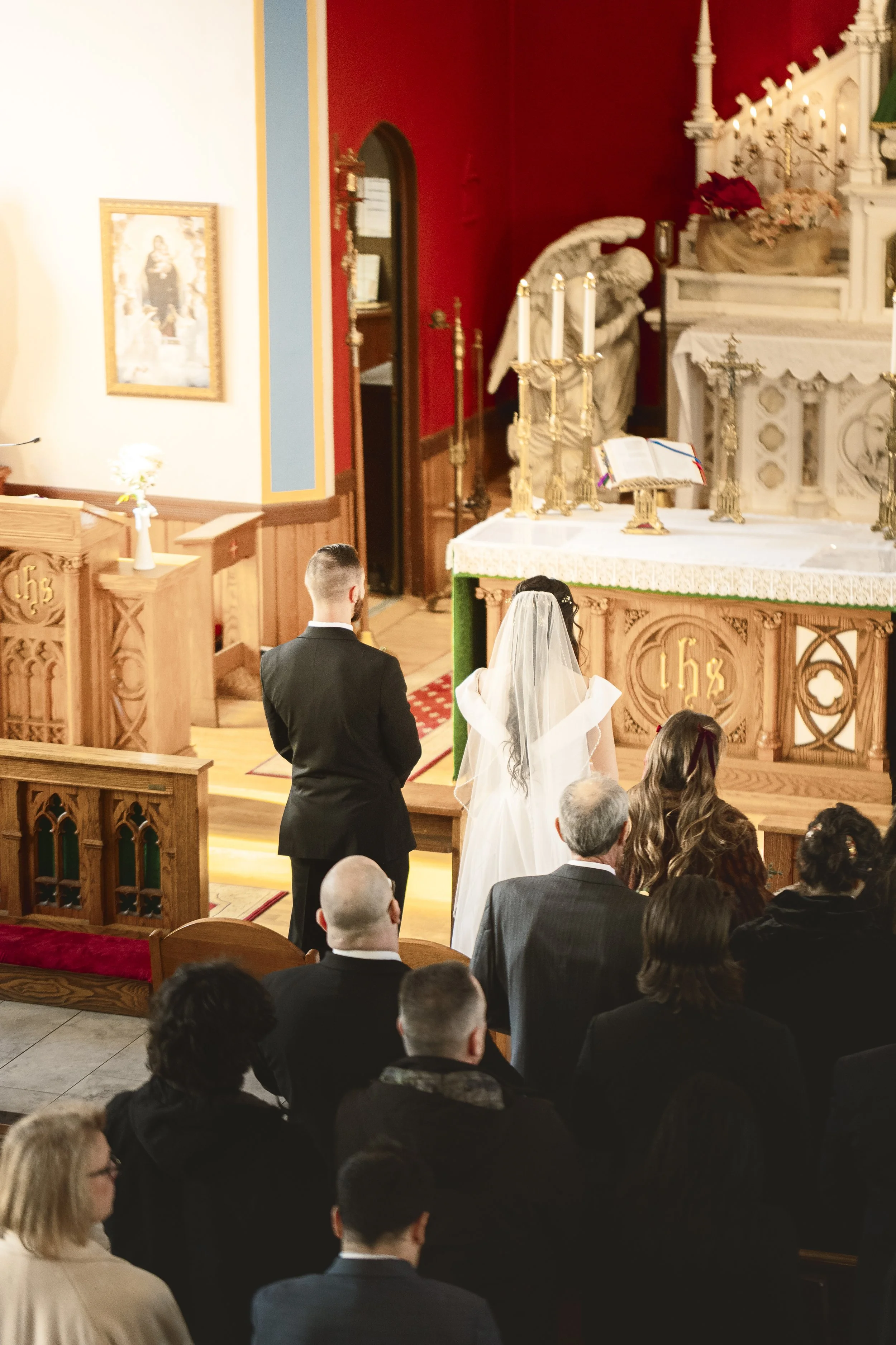 A bride and groom standing during a wedding ceremony inside a church, with guests seated and watching.