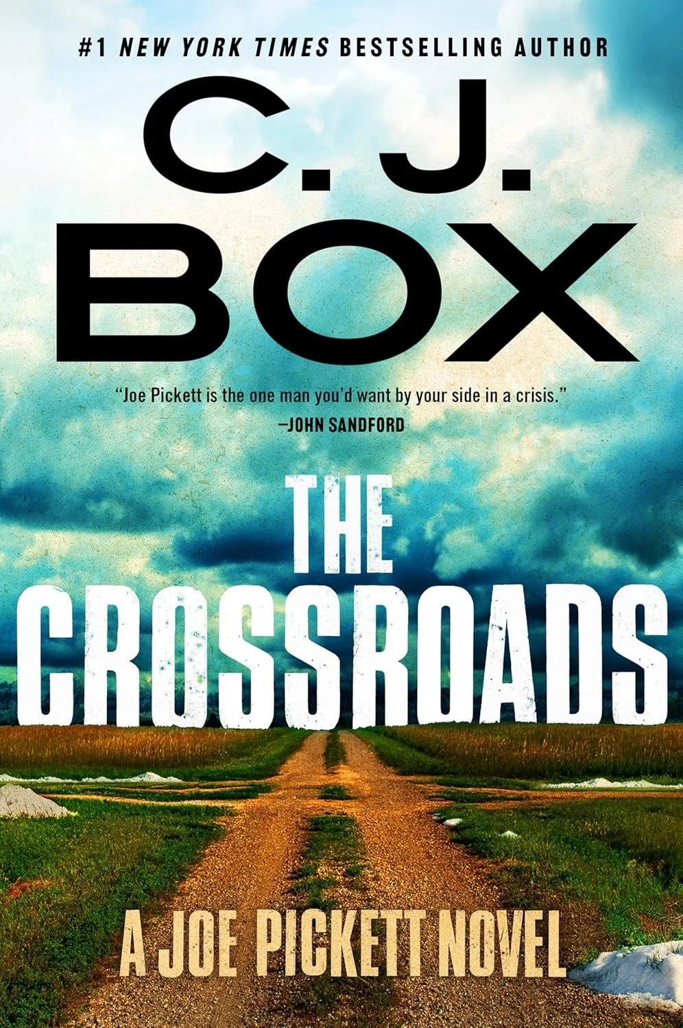 Book cover for 'The Crossroads' by C. J. Box, featuring a dirt road leading through grassy fields under a blue sky with clouds.