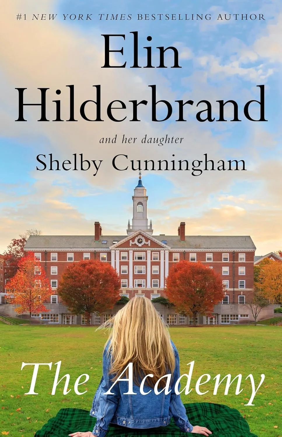 Book cover for 'The Academy' by Elin Hilderbrand and Shelby Cunninghman, featuring a young woman with blonde hair sitting on grass with back to camera, looking at a large, brick academic building with a clock tower, surrounded by trees with autumn fo