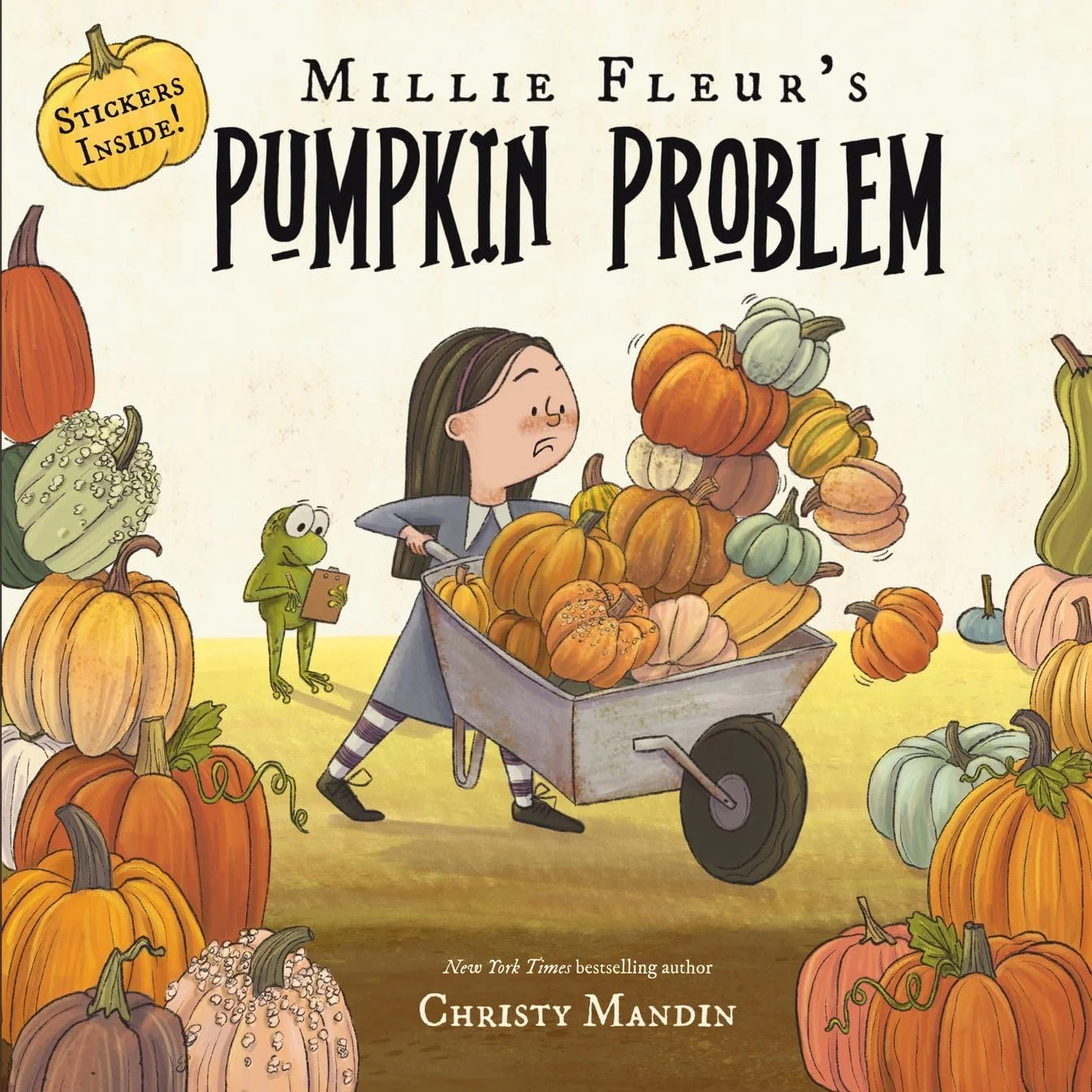 Book cover titled 'Millie Fleur's Pumpkin Problem' featuring a girl pushing a wheelbarrow filled with pumpkins, surrounded by various colorful pumpkins and gourds, with a small green frog reading a book in the background.