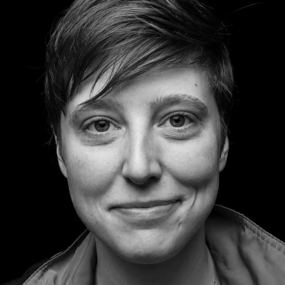 Black and white close-up portrait of a woman with short hair, smiling subtly, looking directly at the camera.