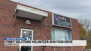 Exterior of a brick building with a sign for 'Funky Solutions' mounted near the top, and a banner at the bottom indicates a food drive for Glens Falls.
