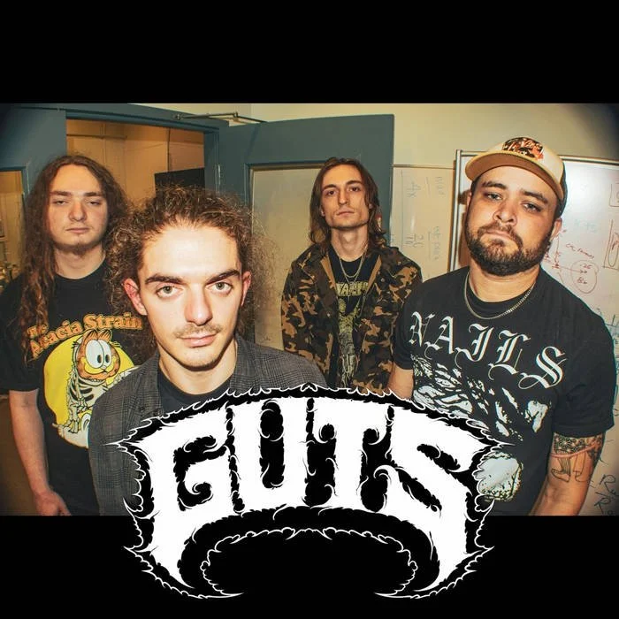 Four young men standing indoors with a whiteboard and a doorway in the background. The front is dominated by a logo with the word 'FUCK' in a bold, gothic font.