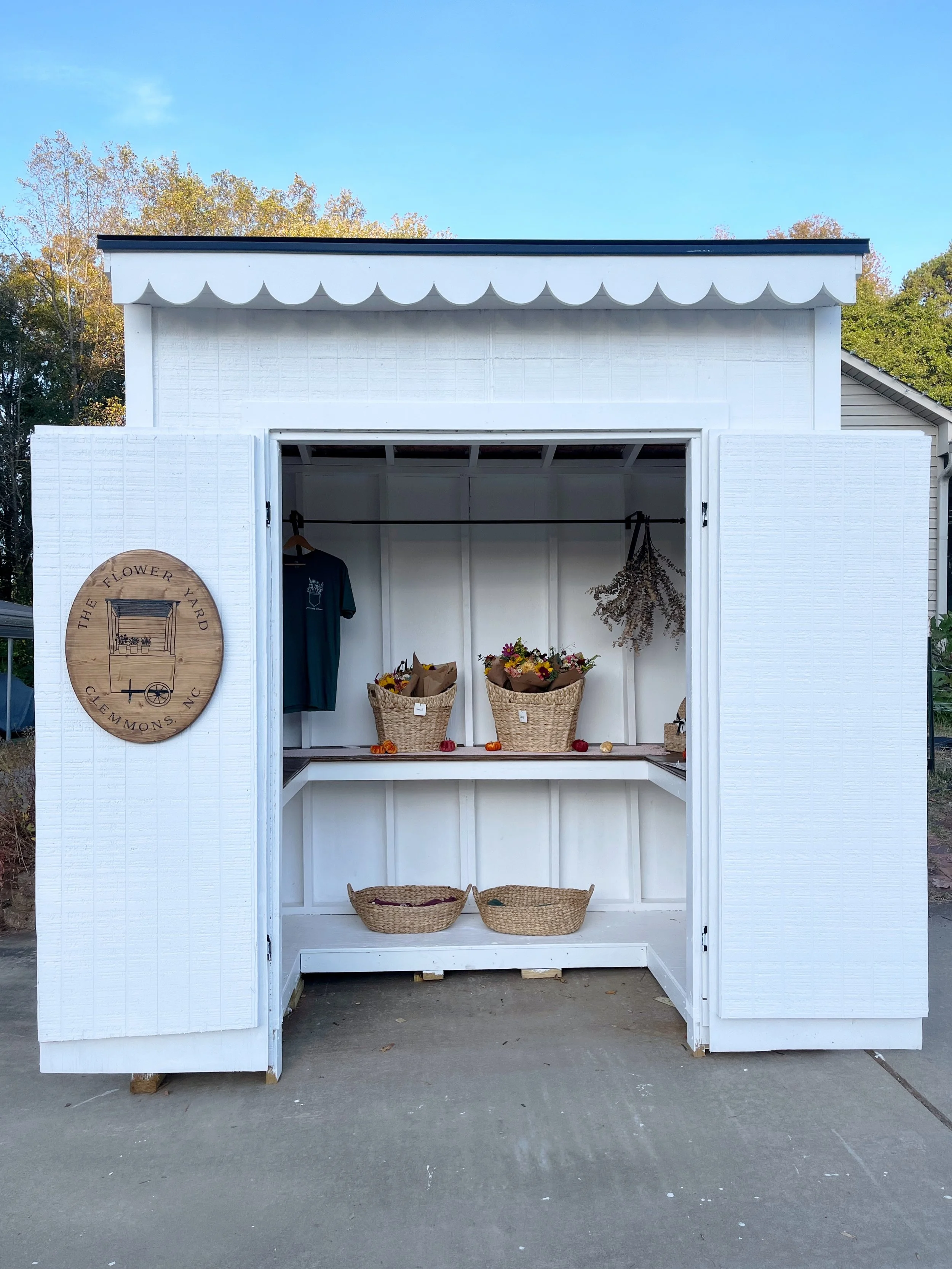 Flower stand with colorful flowers in vases and baskets, a pink sign, and a black mailbox, labeled 'The Flower Yard'.
