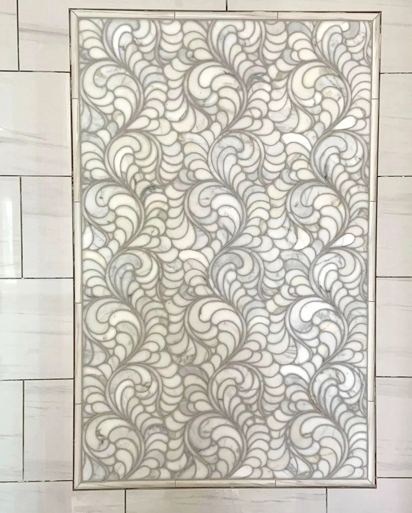 Decorative white tile with intricate gray swirling pattern, inset in a tiled wall.