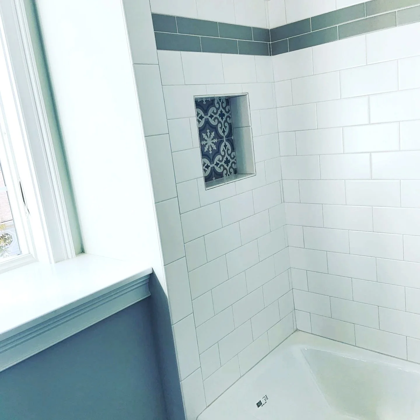 Bathroom shower with white subway tiles, a decorative tile niche, and a window nearby.