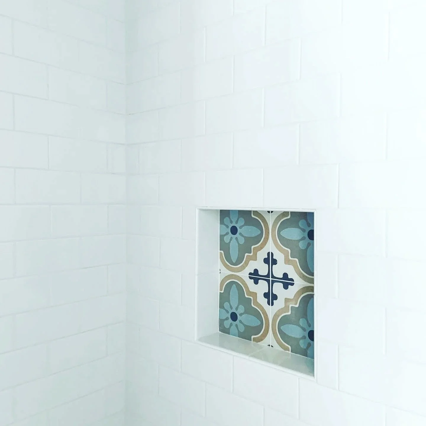 White tiled wall with a decorative tile insert featuring blue, beige, and dark blue patterns.