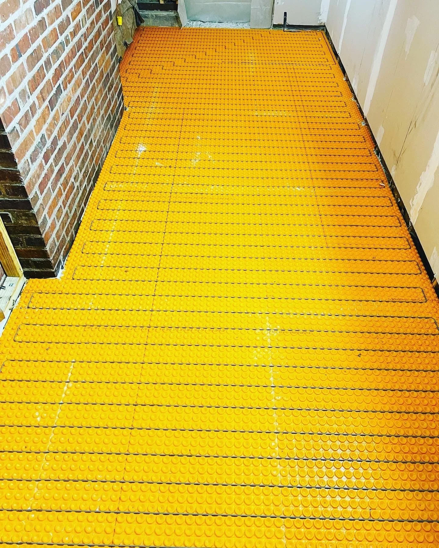 Orange anti-slip flooring tiles on a hallway floor with brick wall on the left and drywall on the right.