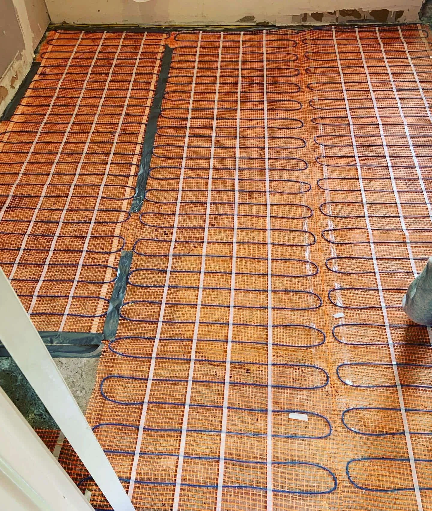 Underfloor heating system installation with orange mesh mat, black heating pipes, and white grid lines on the floor.