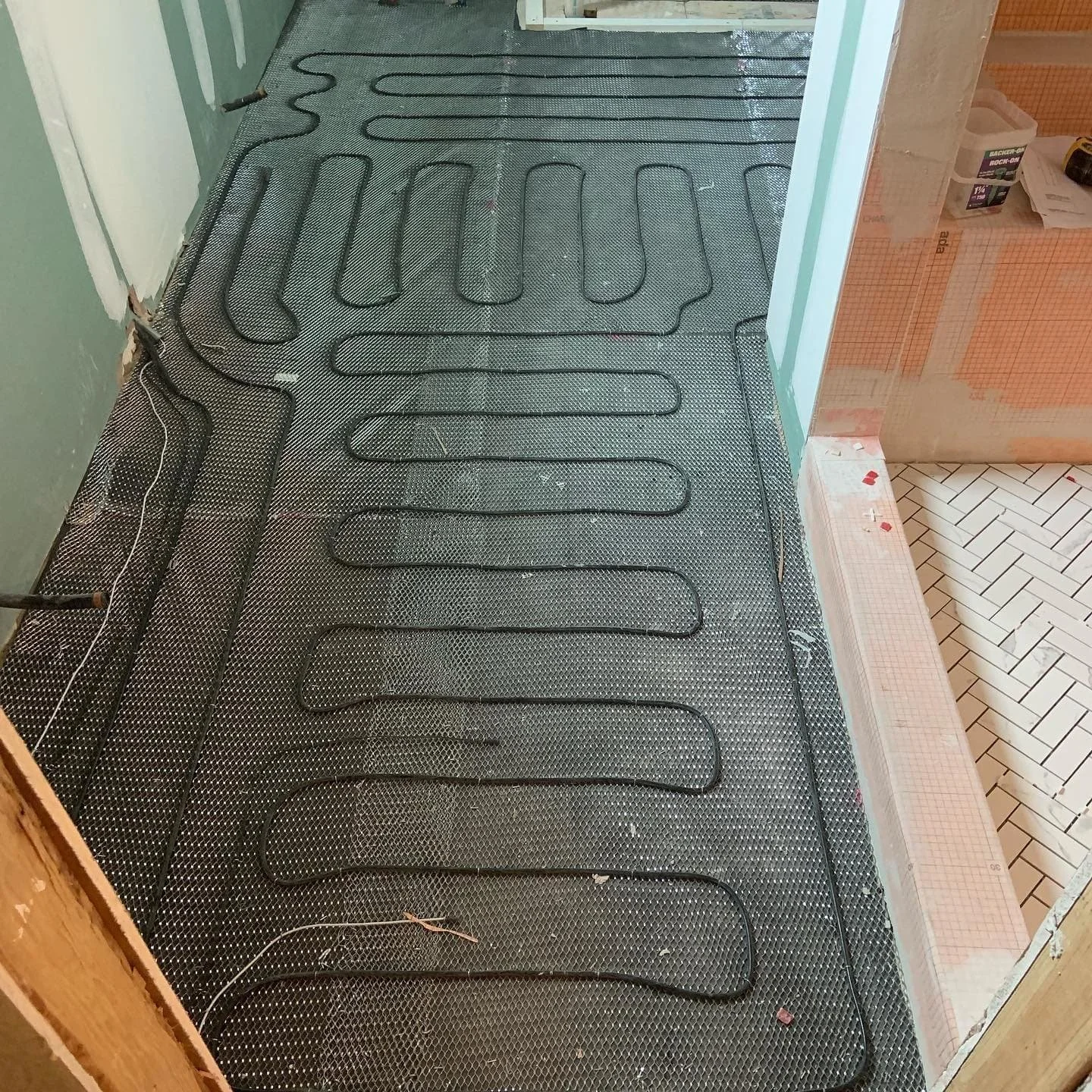 Underfloor heating pipes installed on a floor, with a gray metal mesh surface underneath, in a room under construction.