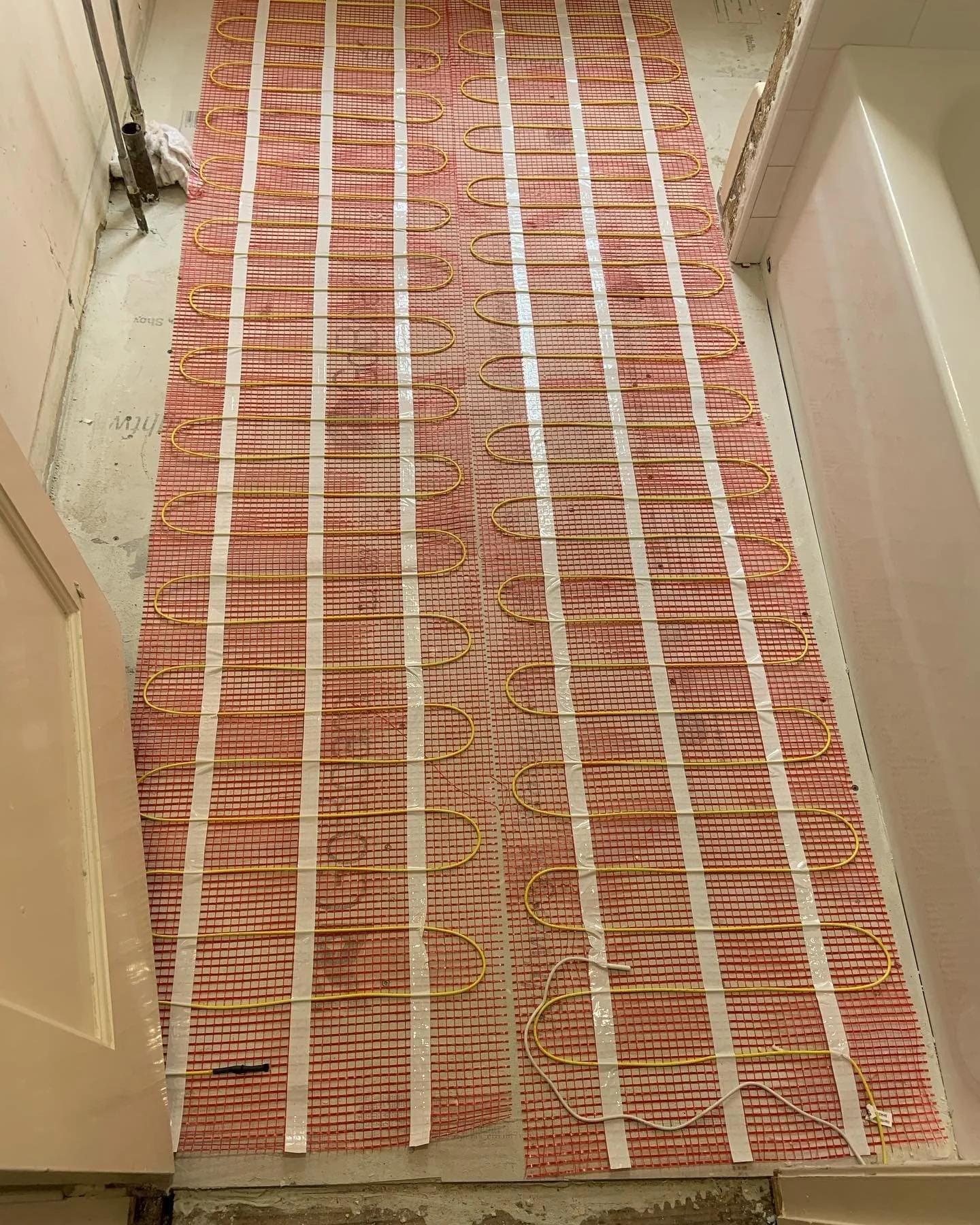 Underfloor heating system installation with electric heating cables laid on the floor in a grid pattern, covered with plastic mesh.