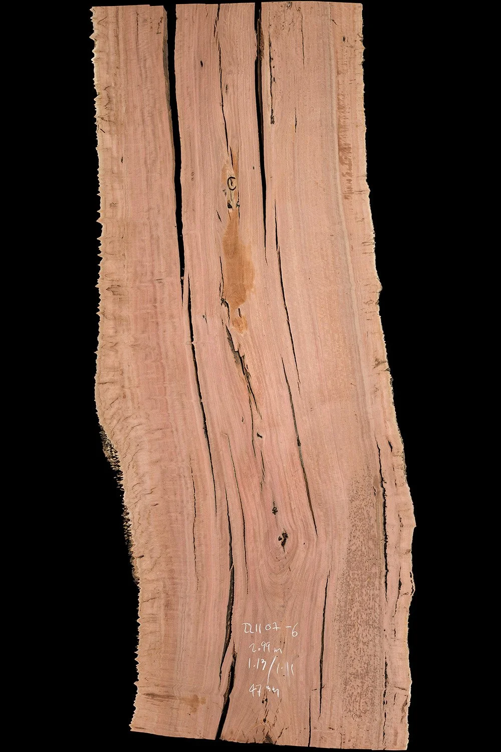 Close-up of a natural, unpolished wooden plank with visible grain, cracks, and markings on a black background.