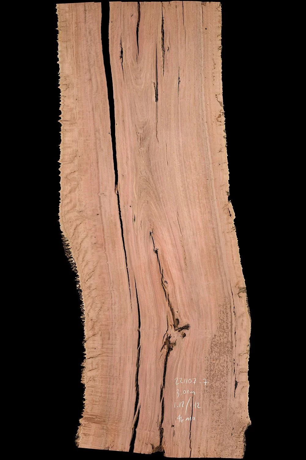 Close-up image of a piece of wood with natural grain patterns and a dark crack running through the middle, with handwritten measurements and notes on the lower right side.