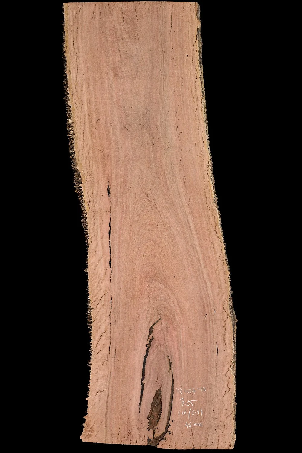 A rectangular slab of pinkish-brown wood with natural grain patterns and rough edges, set against a black background.