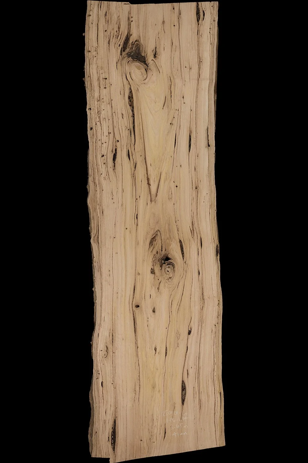 A vertically oriented piece of natural wood with a light tan color and distinctive grain patterns, set against a black background.