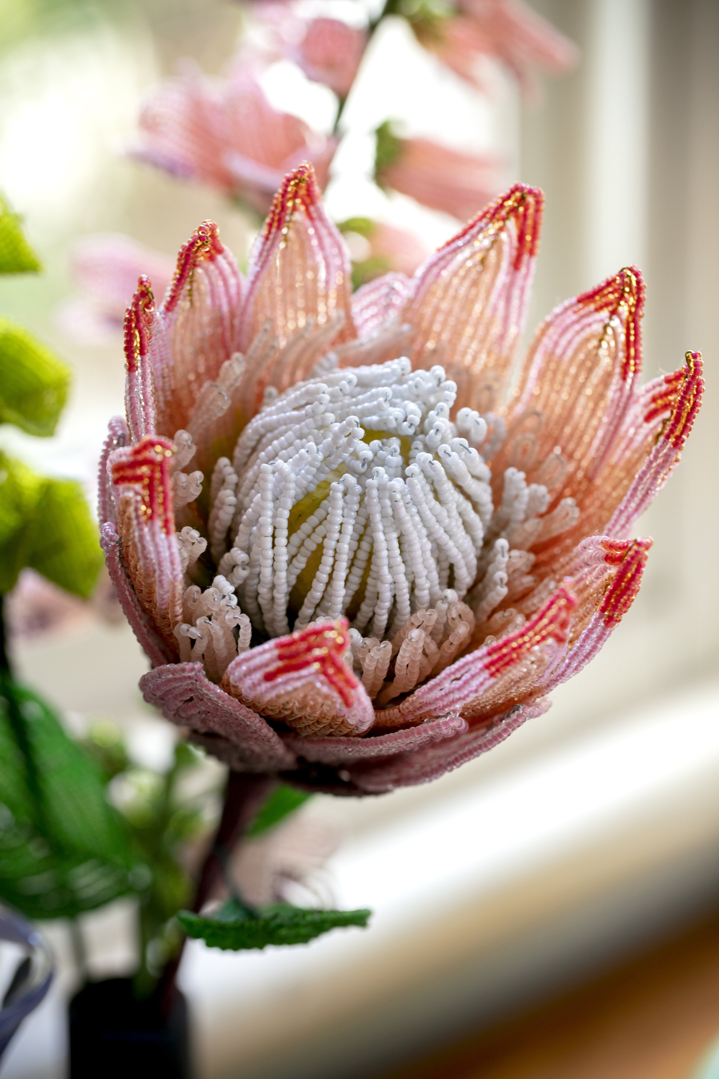 Close-up of a beaded artificial flower resembling a pink protea with intricate beadwork and fabric petals.