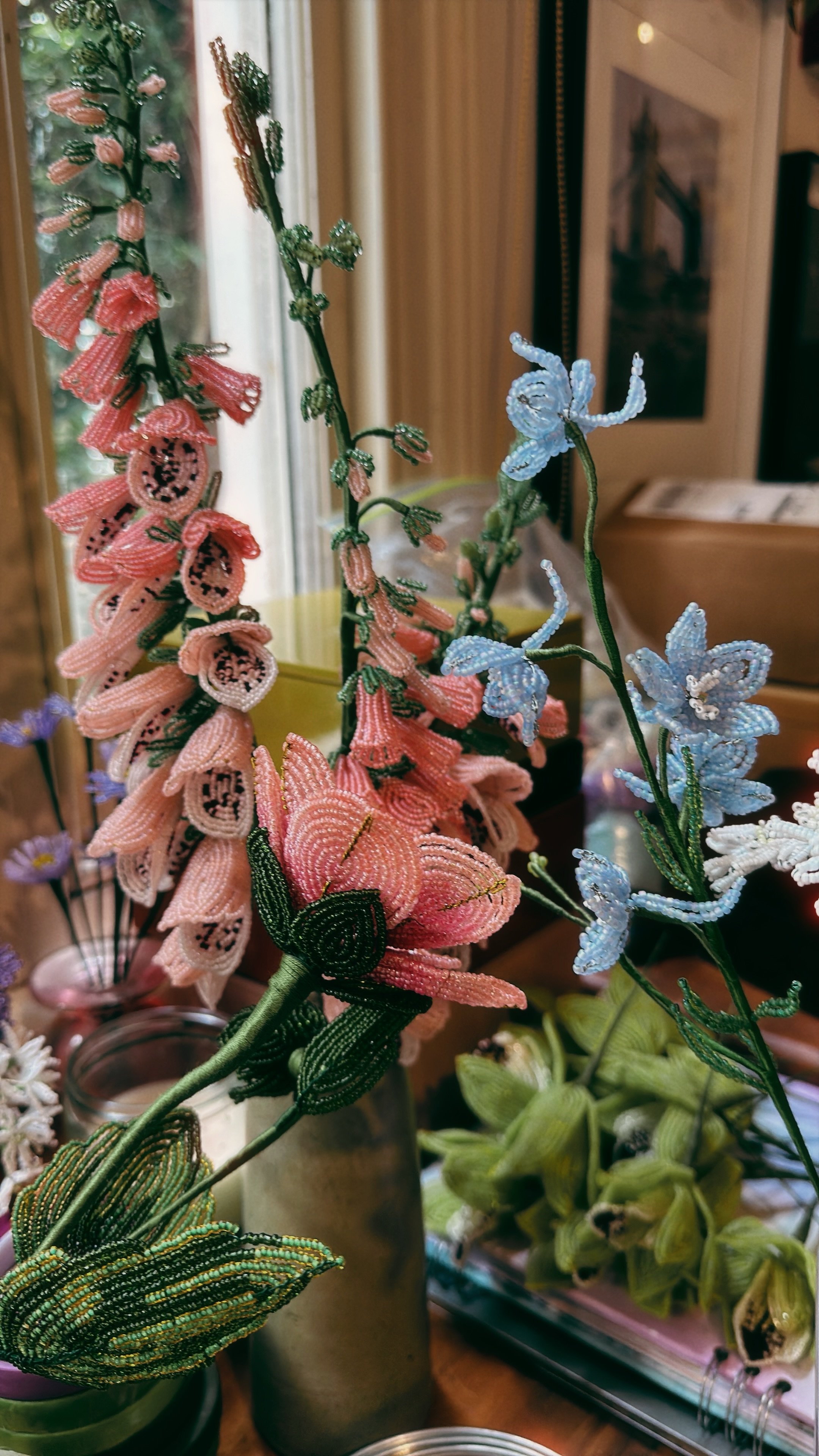 Colorful beaded flower and butterfly decor arrangements on a table near a window.