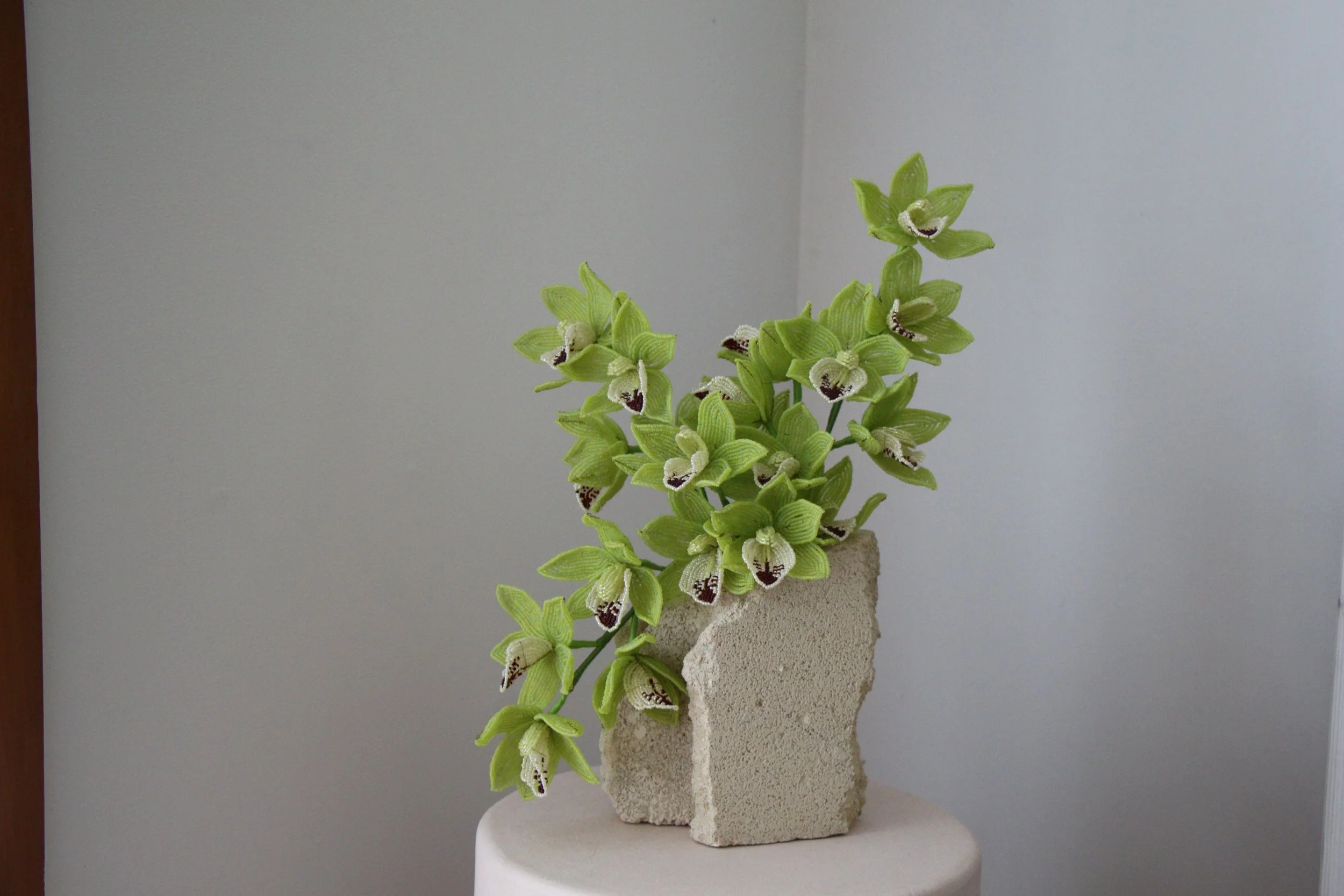 Artificial green orchid flowers in a concrete-like vase on a round white pedestal.