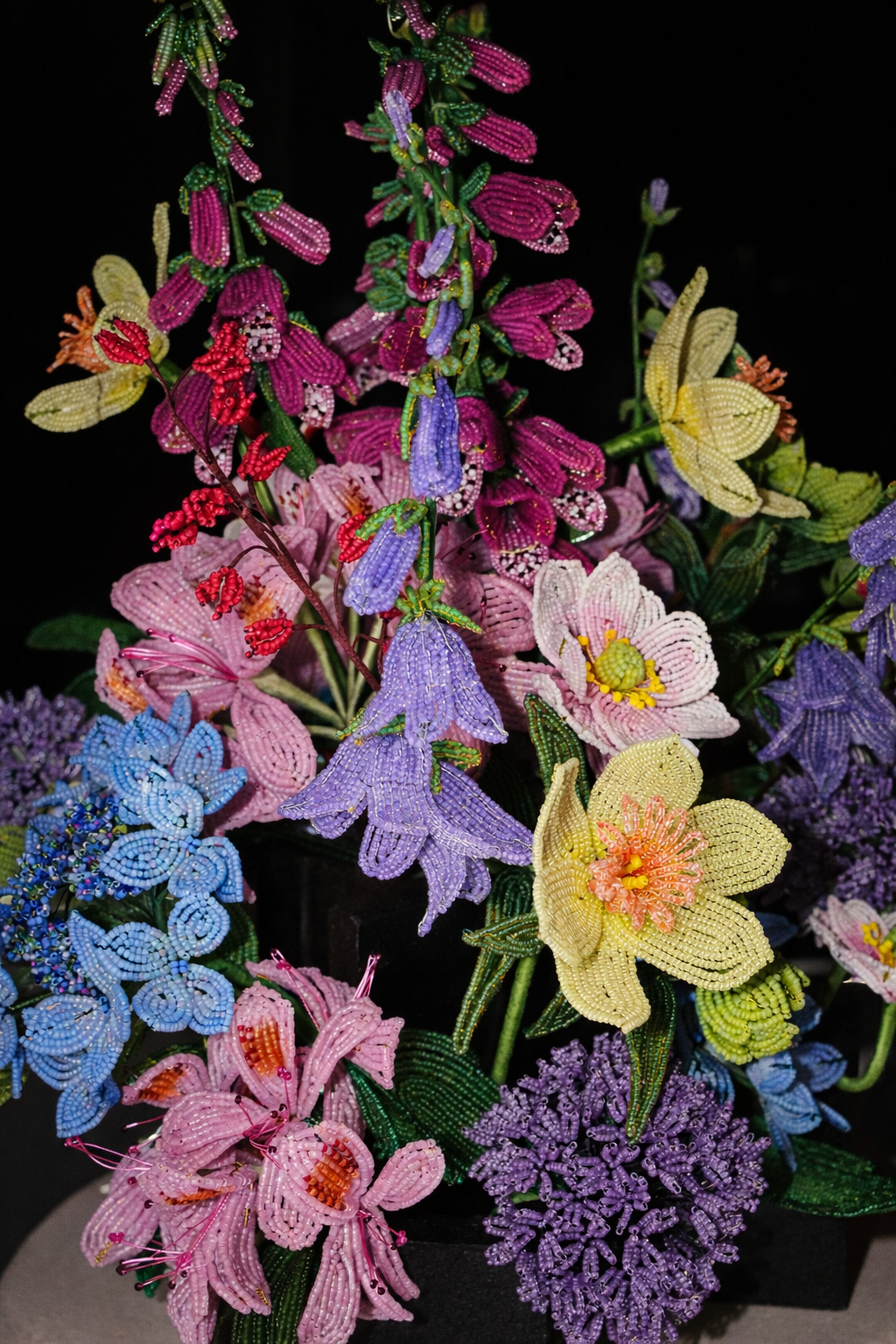 Colorful beaded floral sculpture by Hark Handmade with purple, pink, yellow, blue, and red flower beads on black background.