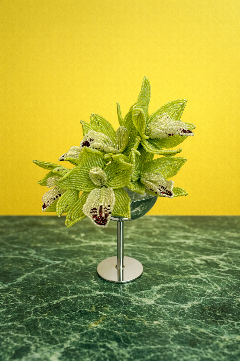Artificial green cactus plant in a glass container on a green marble surface with a yellow background