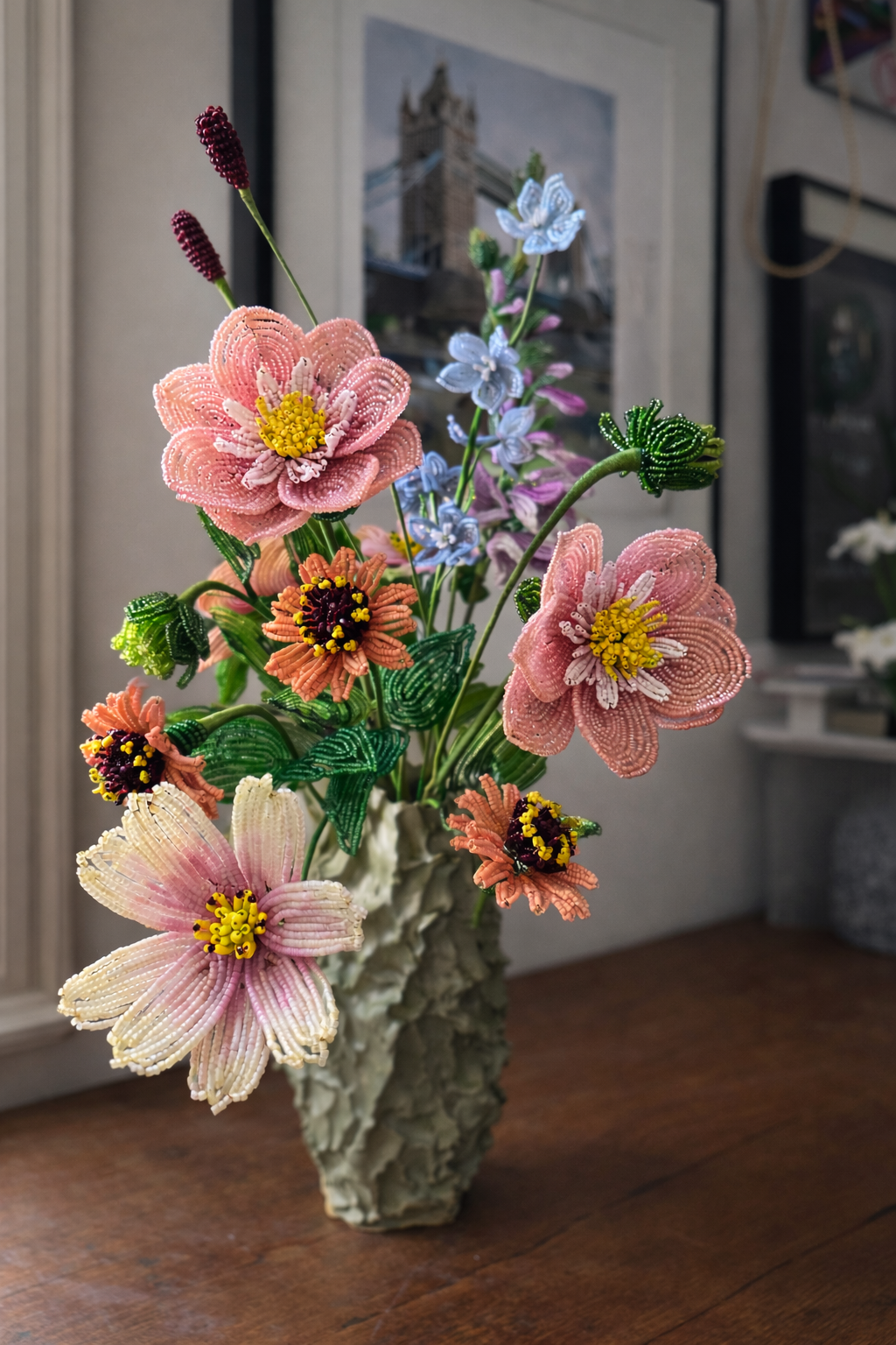 Beaded flower bouquet in a textured ceramic vase on a wooden table, with a framed picture and a microwave in the background.
