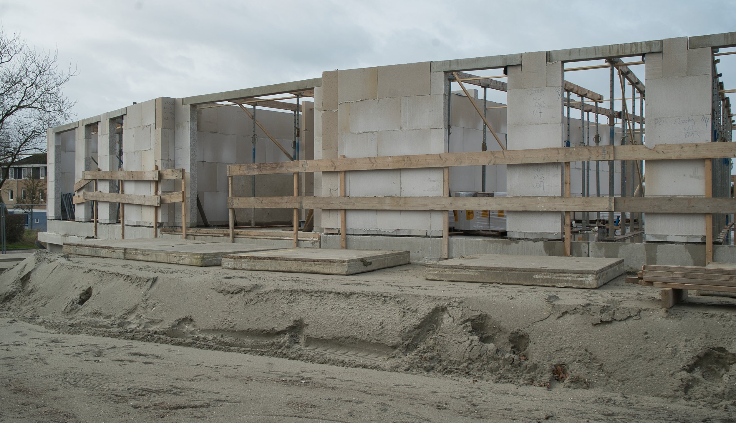 Op de tijdelijke betonplaten rond het gebouw worden de prefab balkons afgesteund.