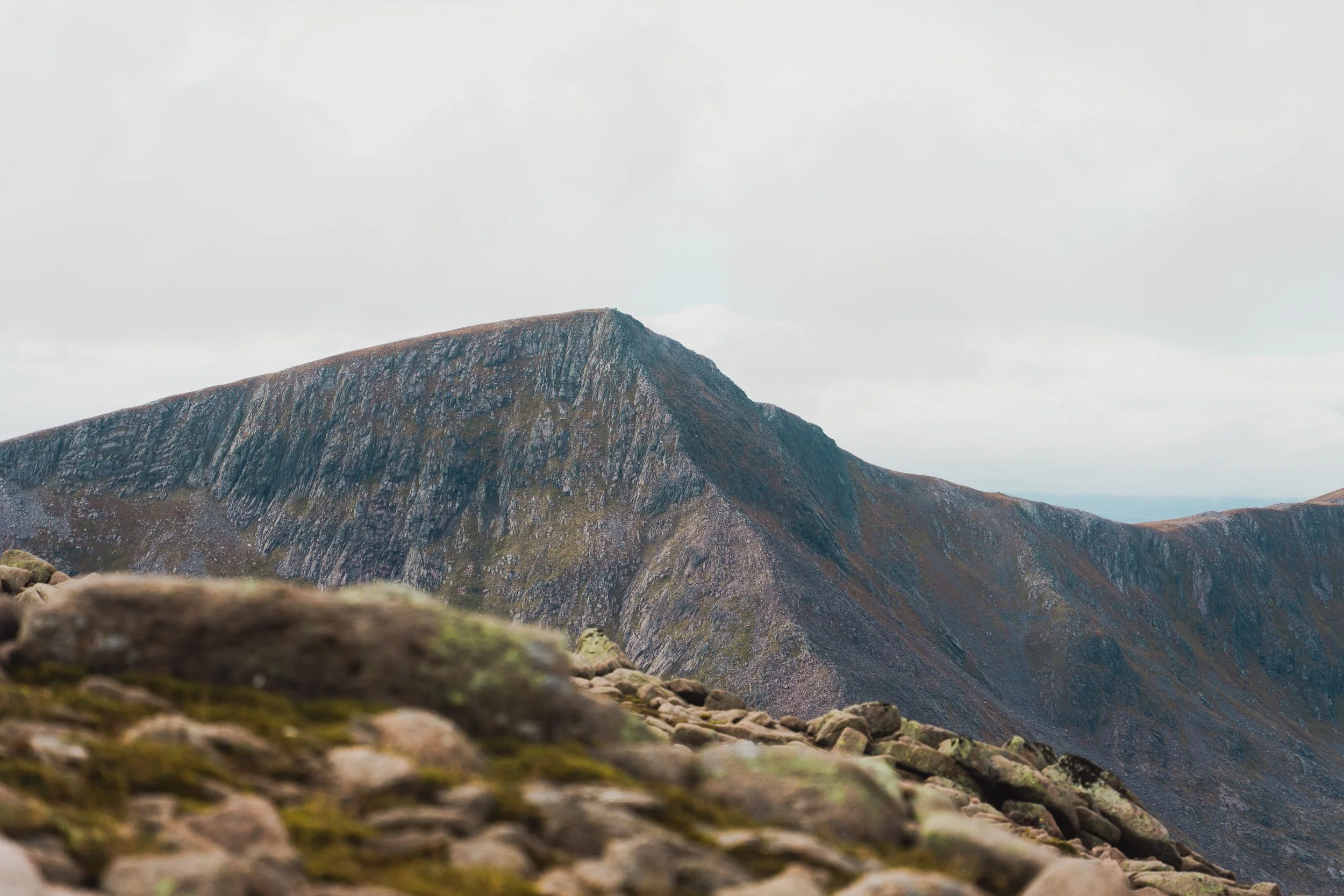 A rugged mountain with steep rocky slopes and a cloudy sky above.