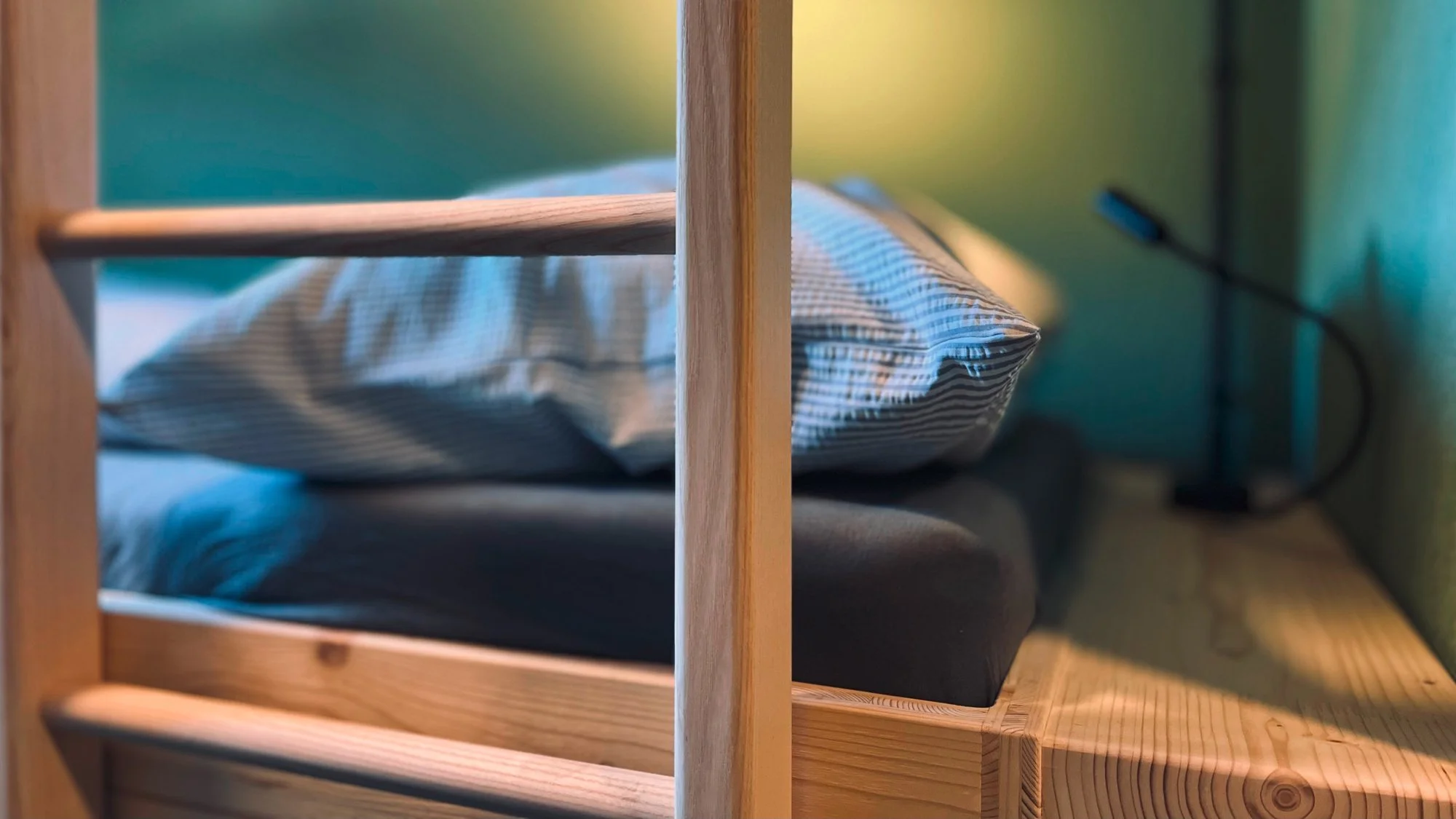 Bett mit Kissen und Decke, im Hintergrund eine Nachttischlampe und ein Nachttisch.