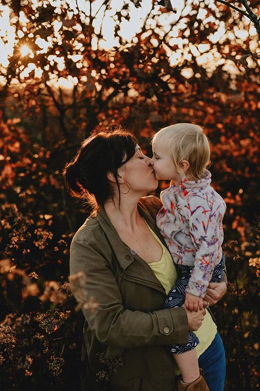 a mom kisses her toddler daughter on top of a mountaintop in western north carolina during a family photo shoot
