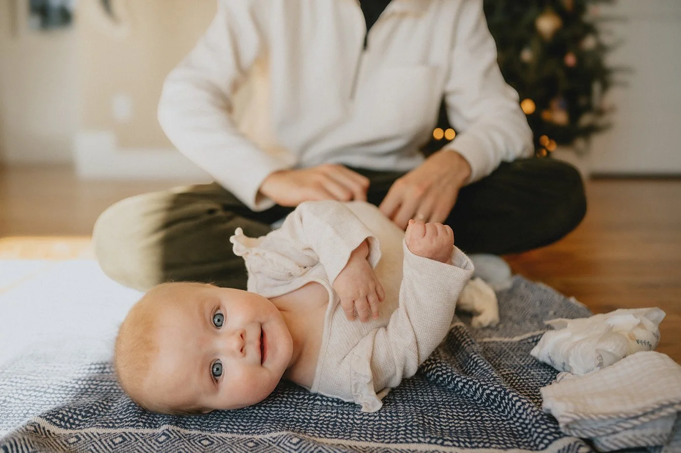 A beautiful blue eyed baby smiles at the camera as her dad dresses her, during a documentary family photography session in North Carolina.