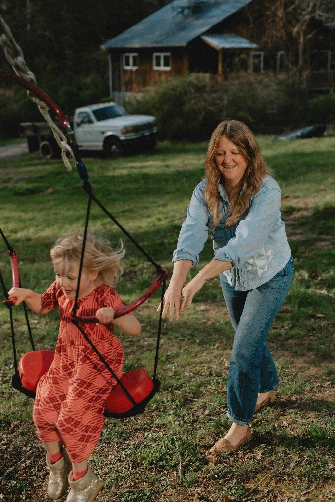 A mother of a blonde haired four year old pushes her child in the swing in the back yard during a spring photo shoot.