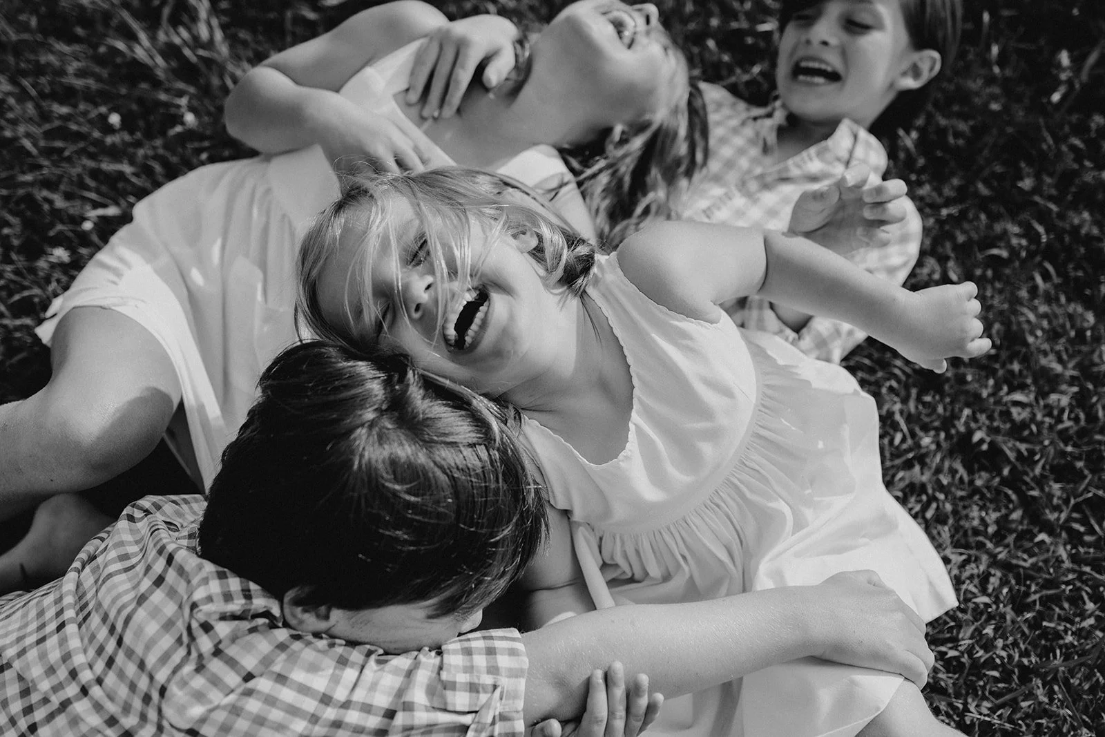 Four children lying and playing on the grass, laughing and having fun together.