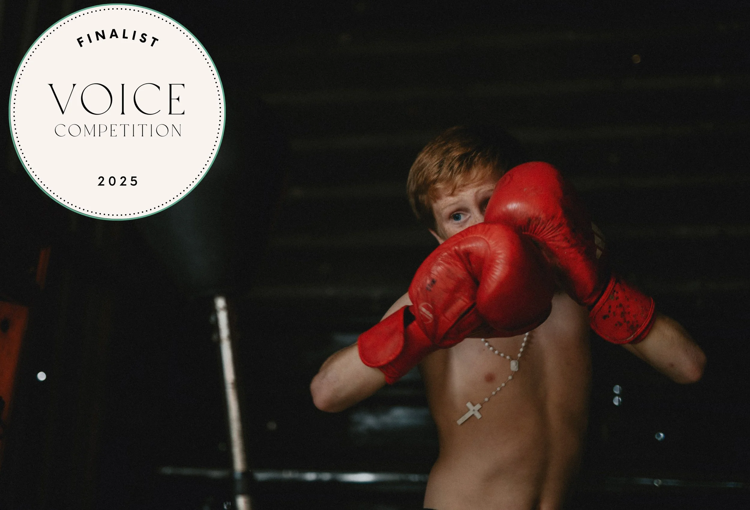 A young shirtless boy with red boxing gloves and a cross necklace is in a boxing stance, raising fists in a dark setting with a circular logo in the top left corner that reads "Finalist Voice Competition 2025".