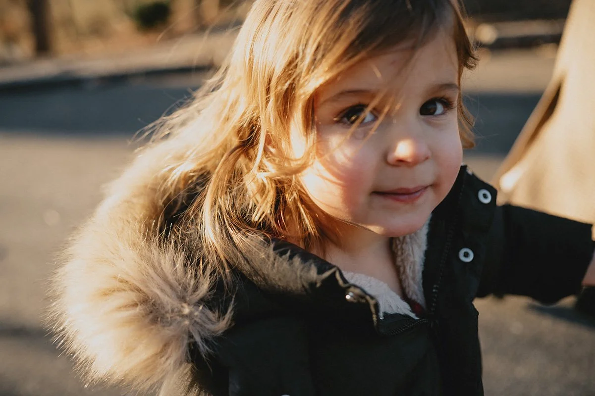 A little girl smiles up at the camera with a tear in her eye and warm, cinematic tones during a family photography session, the parents wanted family pictures.